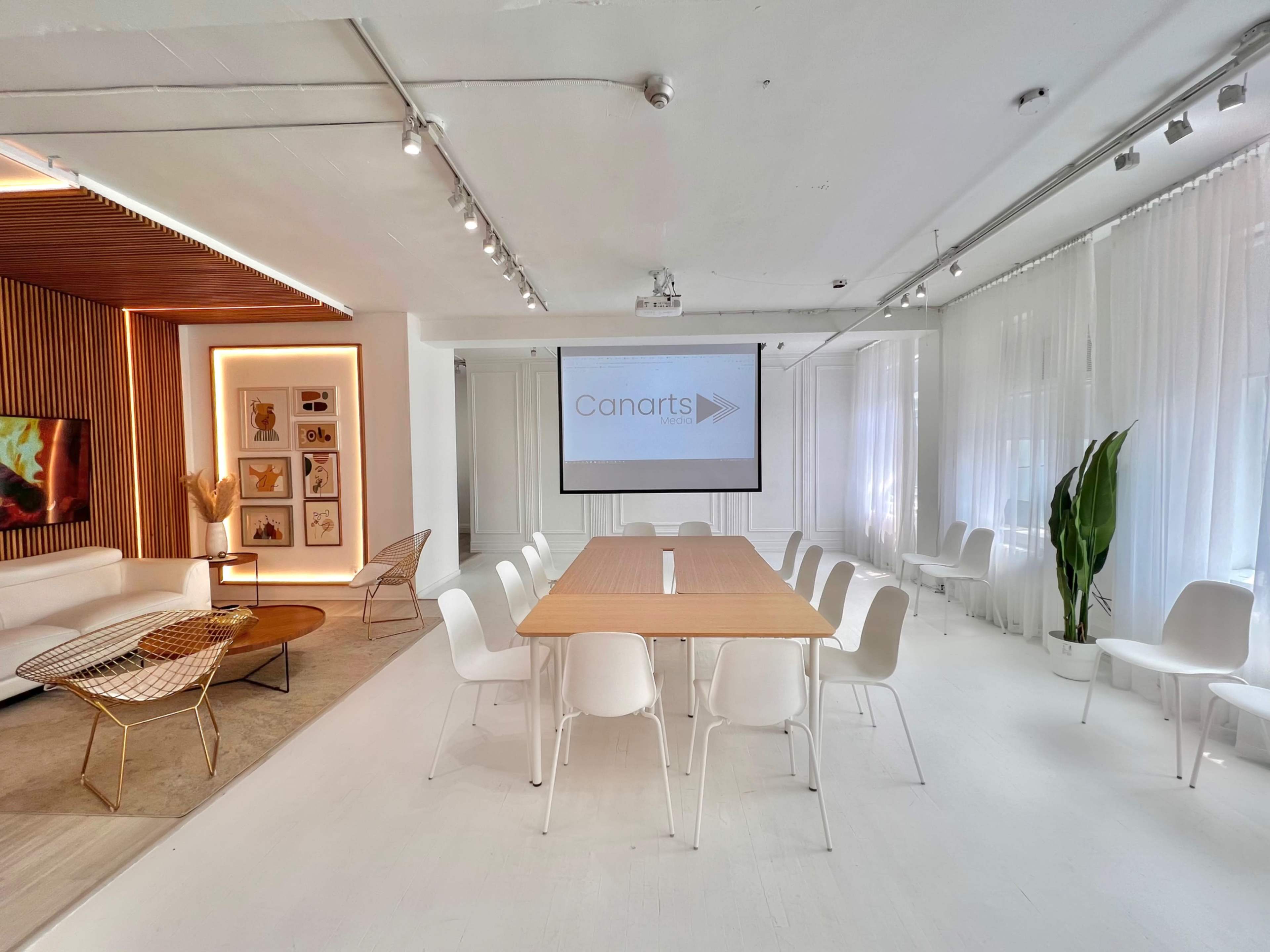 A modern conference room features a large wooden table surrounded by white chairs, with a projector screen displaying "Canarts" on one wall.