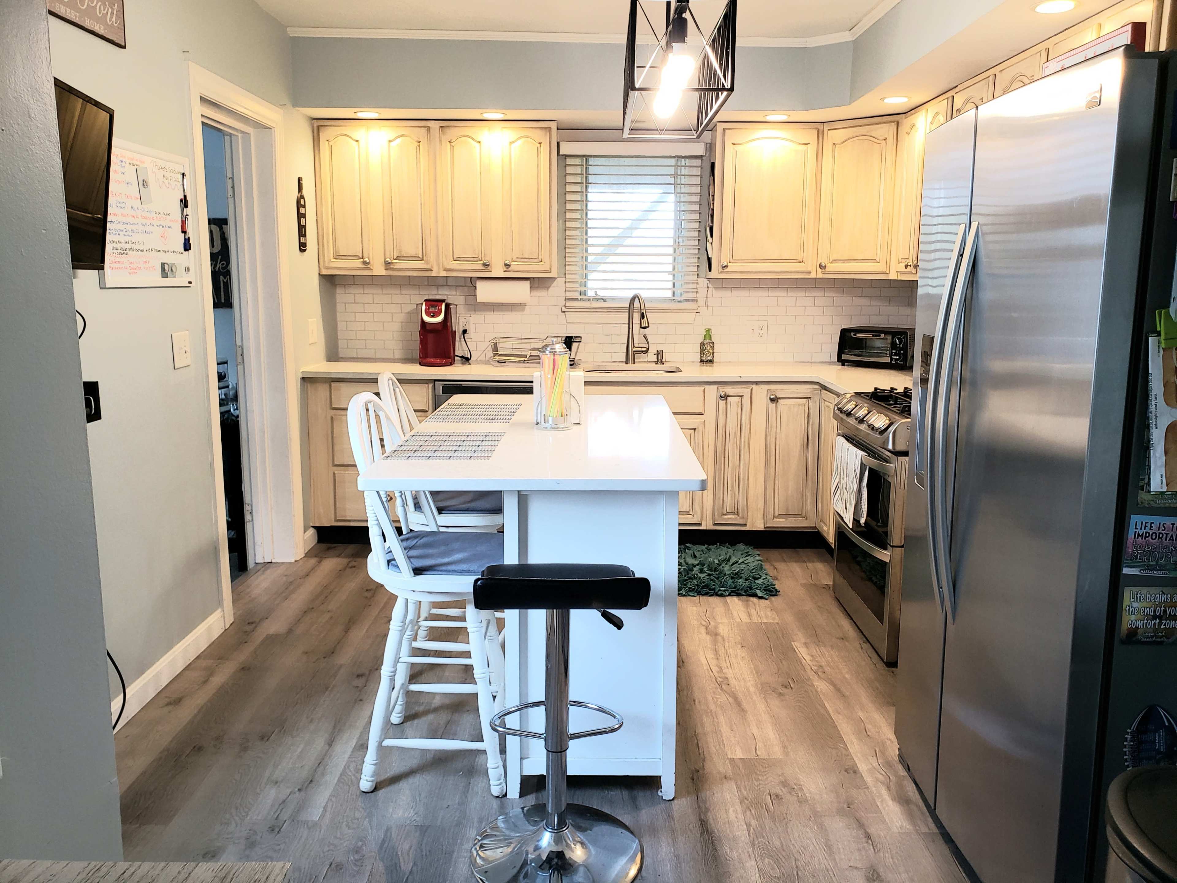 A modern kitchen with light-colored cabinets, stainless steel appliances, and a central island with bar stools.
