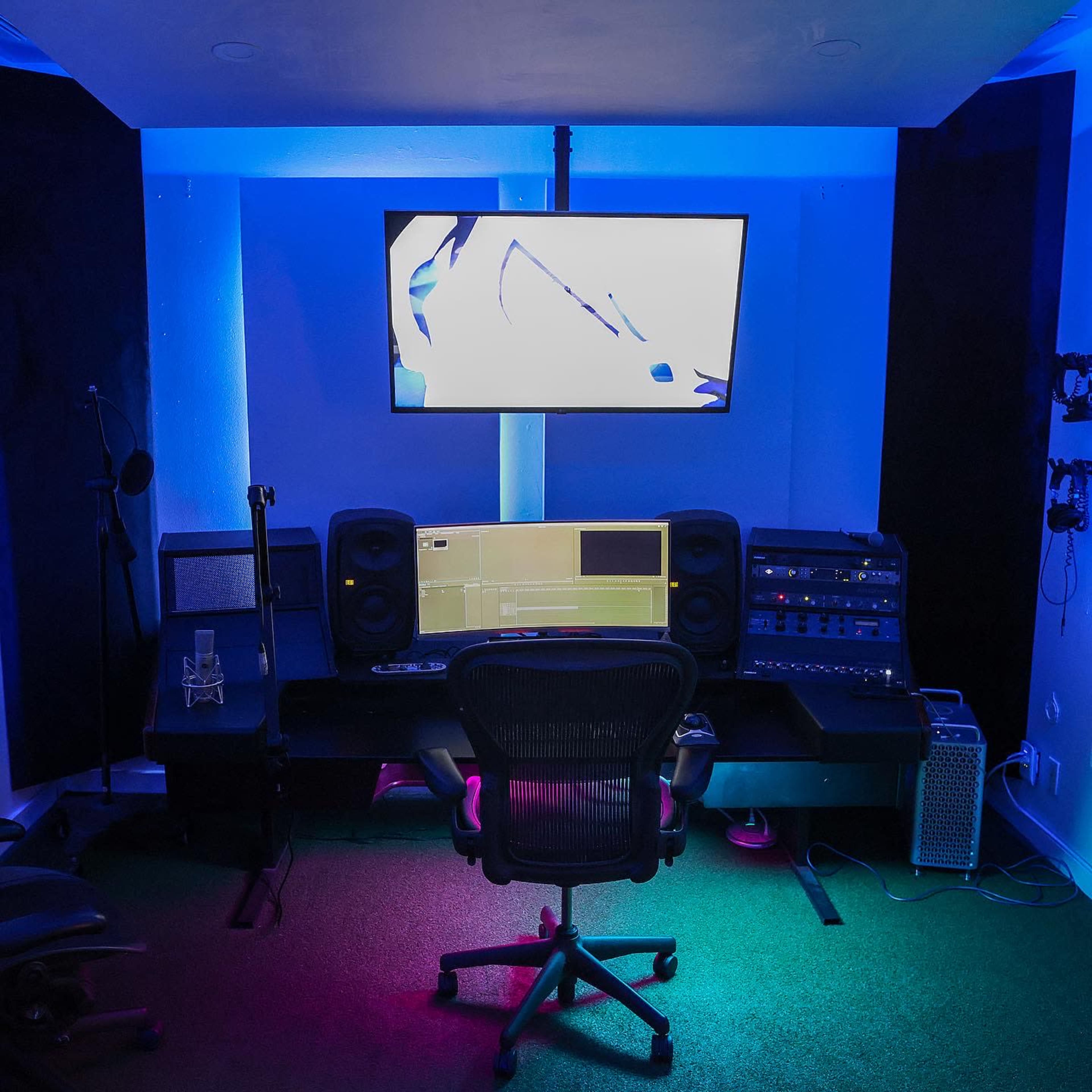 A modern audio and video editing studio featuring a computer workstation, large monitor, and colorful ambient lighting.