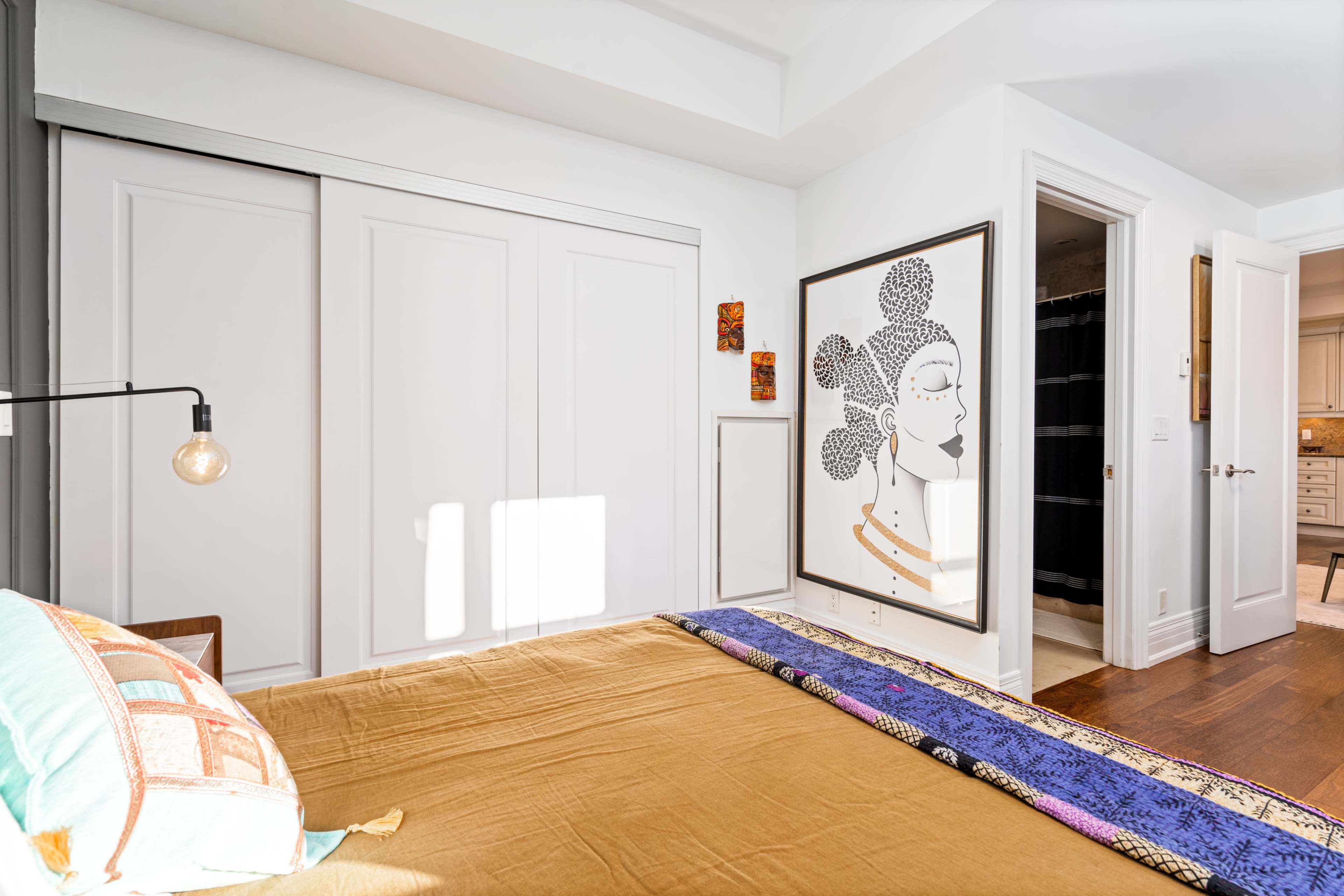 A bright bedroom with a large bed, a wall art piece featuring a woman's face, and two closed closets.