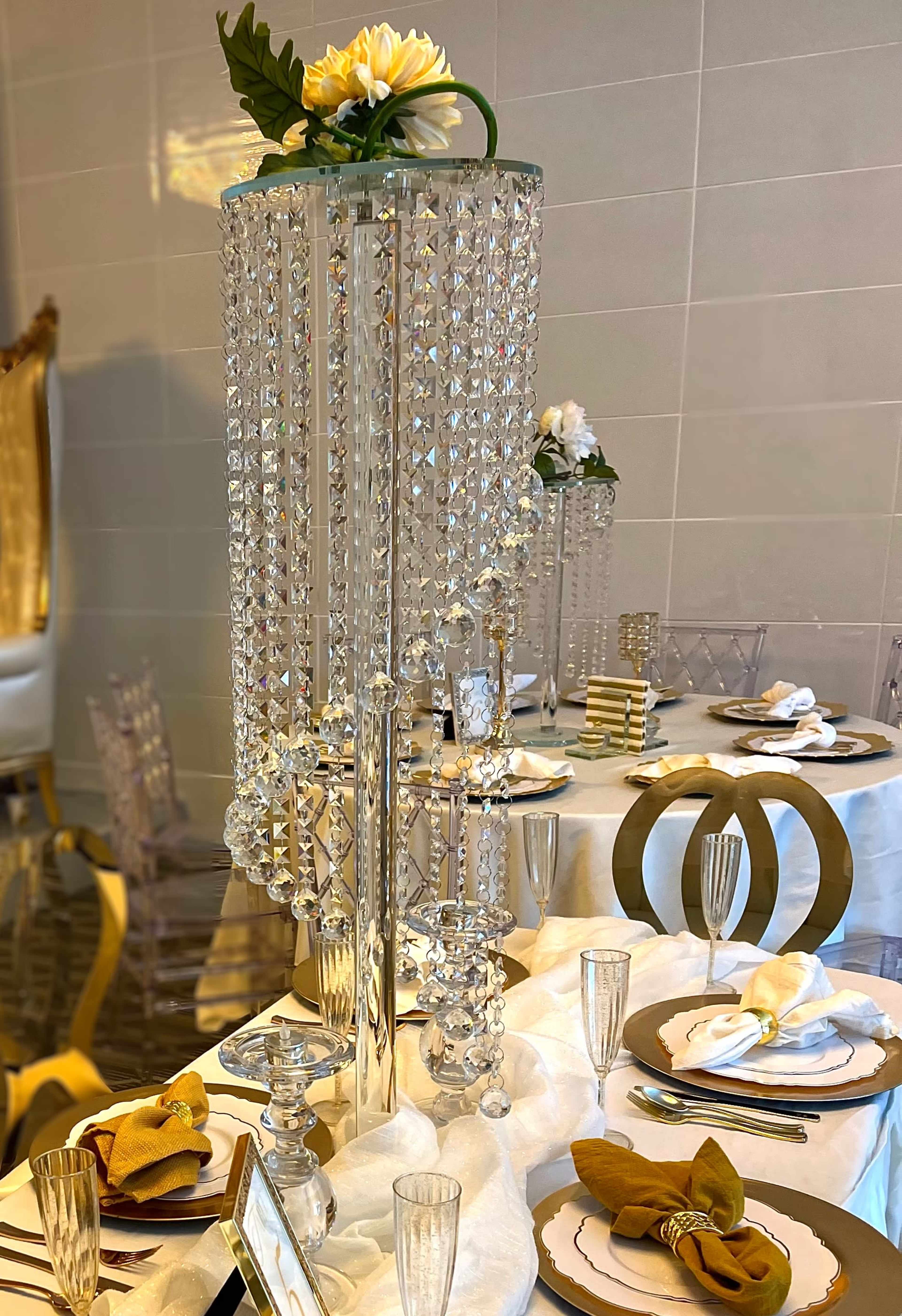 A tall crystal centerpiece adorned with a flower sits on a beautifully arranged dining table featuring elegant tableware and glassware.