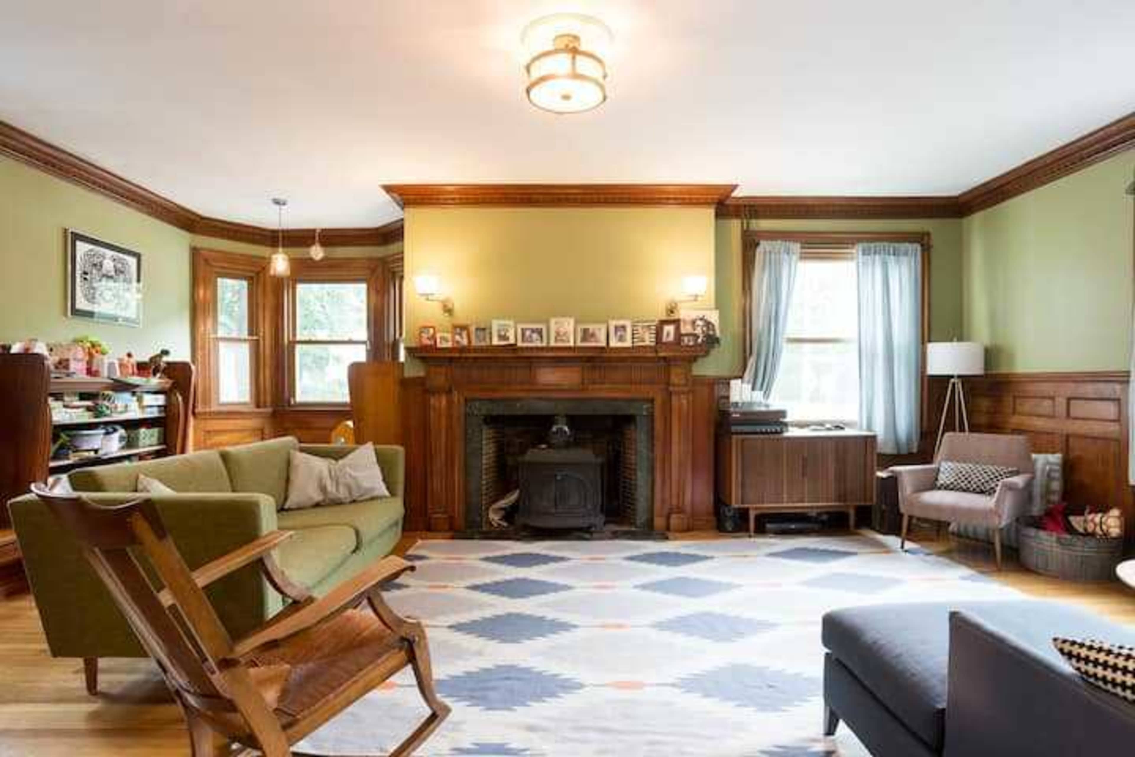 The living room features a green color scheme with wooden paneling, a fireplace, a patterned rug, and various seating arrangements.