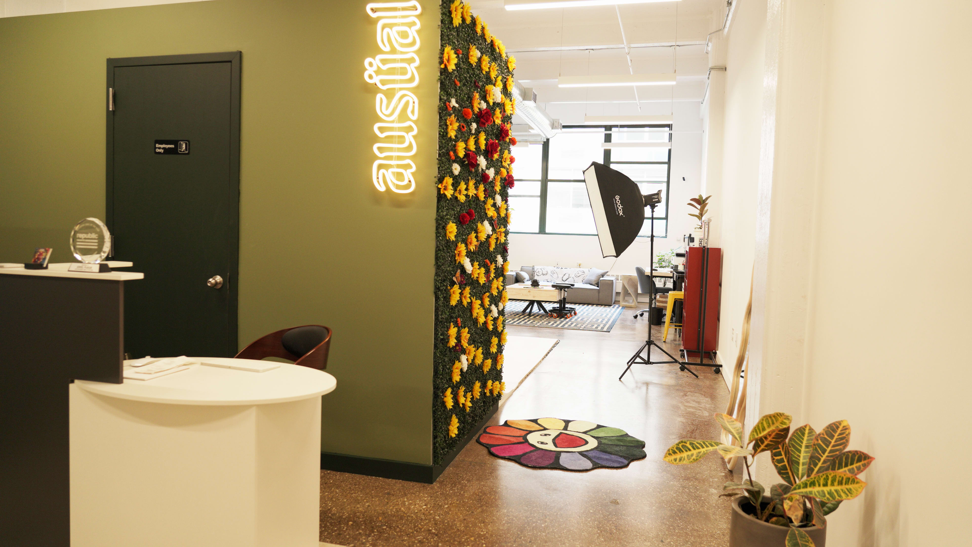 A modern office entrance featuring a reception desk, a vibrant flower wall, and a cozy seating area in the background.