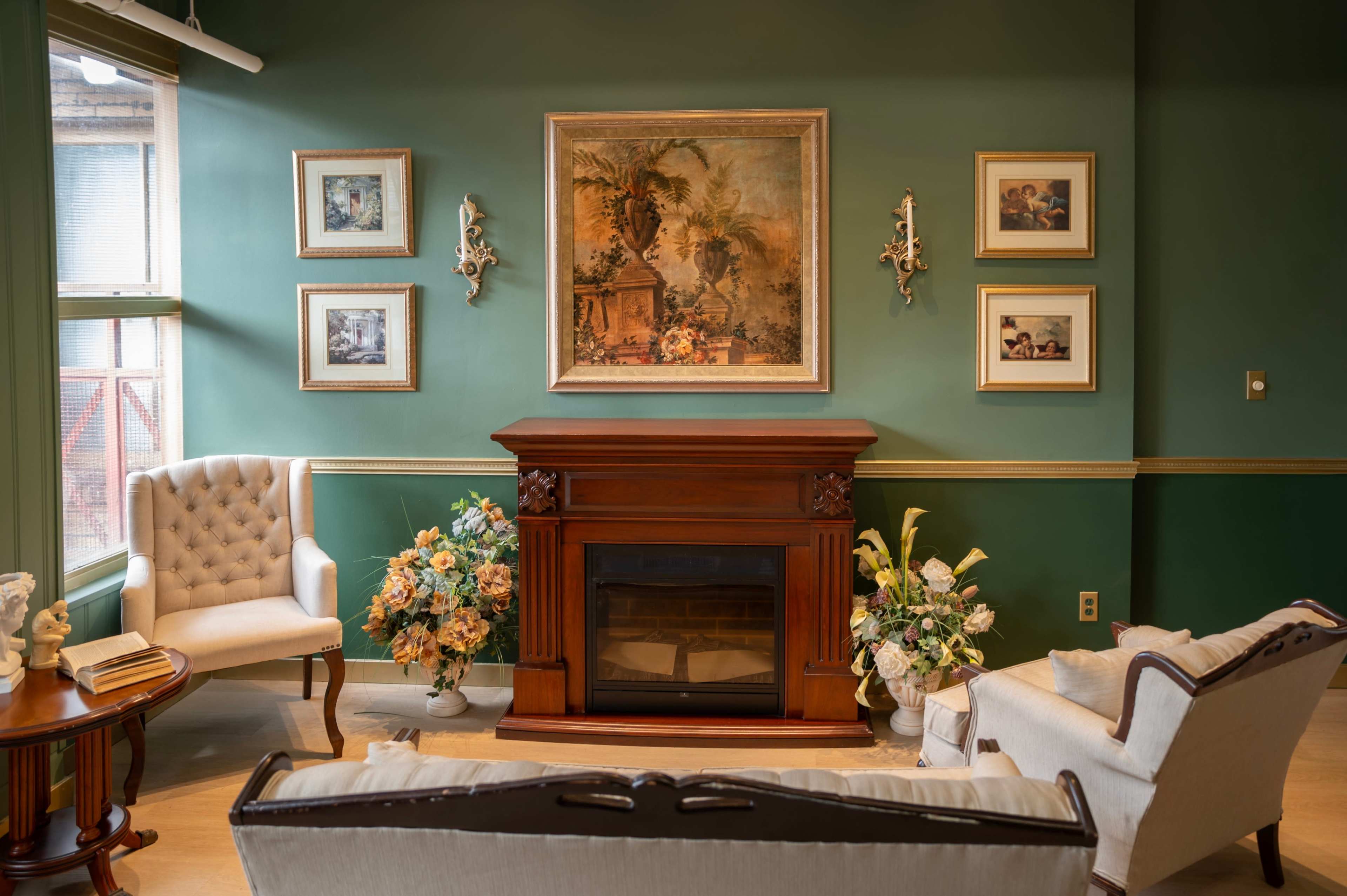 A cozy living room with a fireplace, decorated walls, and floral arrangements beside two upholstered chairs.