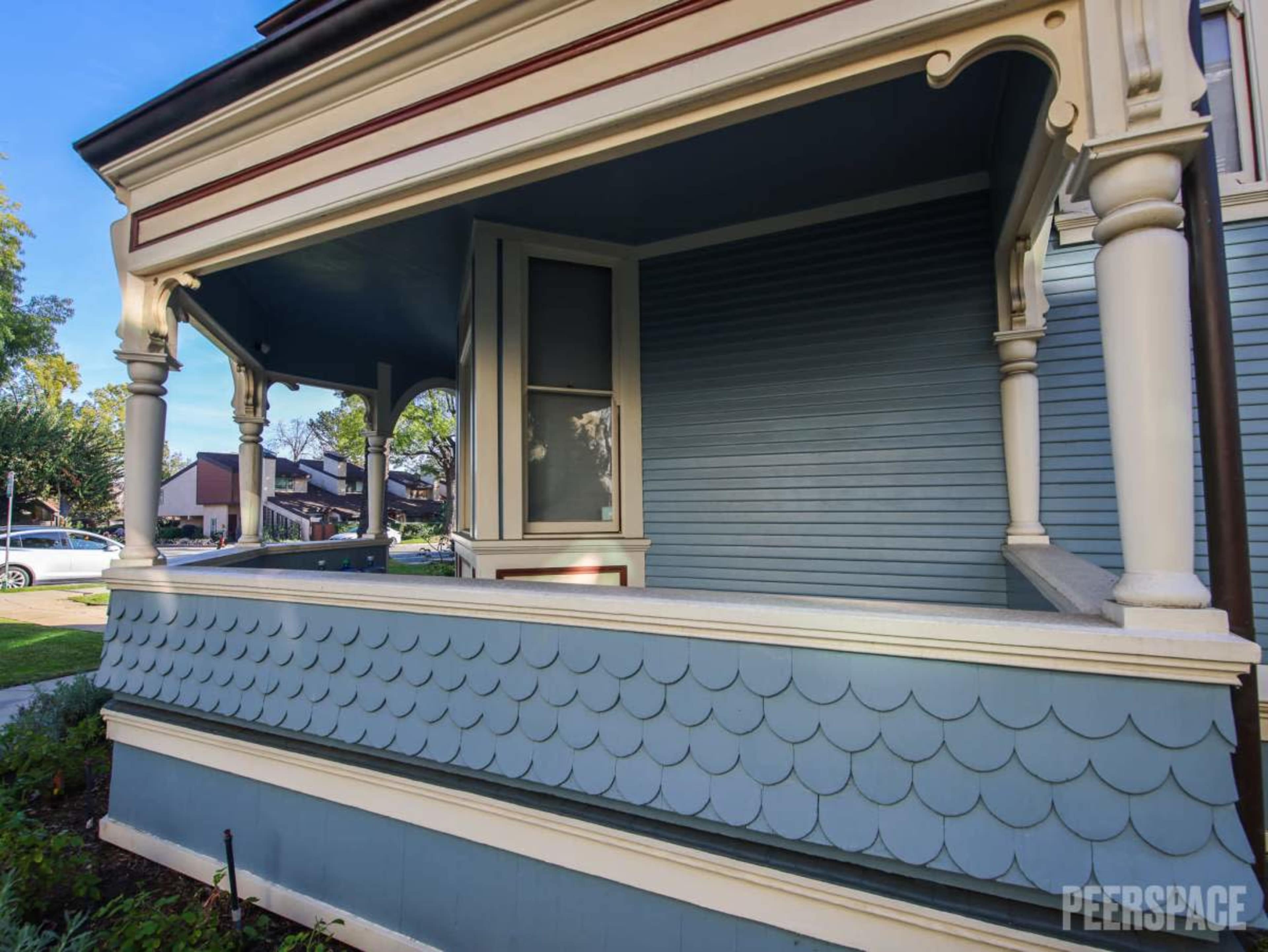 The image shows a Victorian-style house with a blue exterior, featuring a decorative porch and scalloped trim.