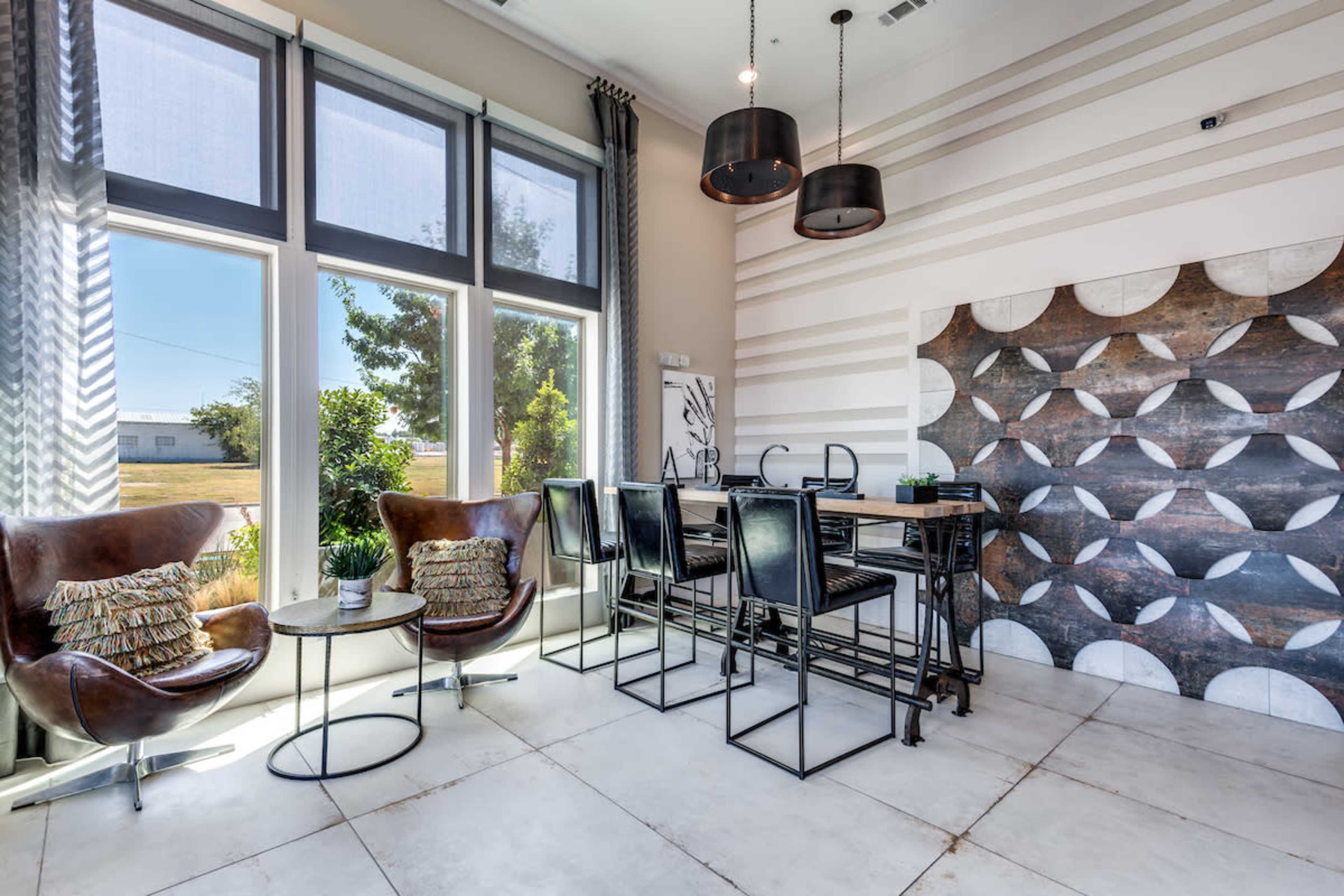 A modern dining area featuring two leather chairs, a small table, and a large rectangular dining table against a wall with a geometric design.