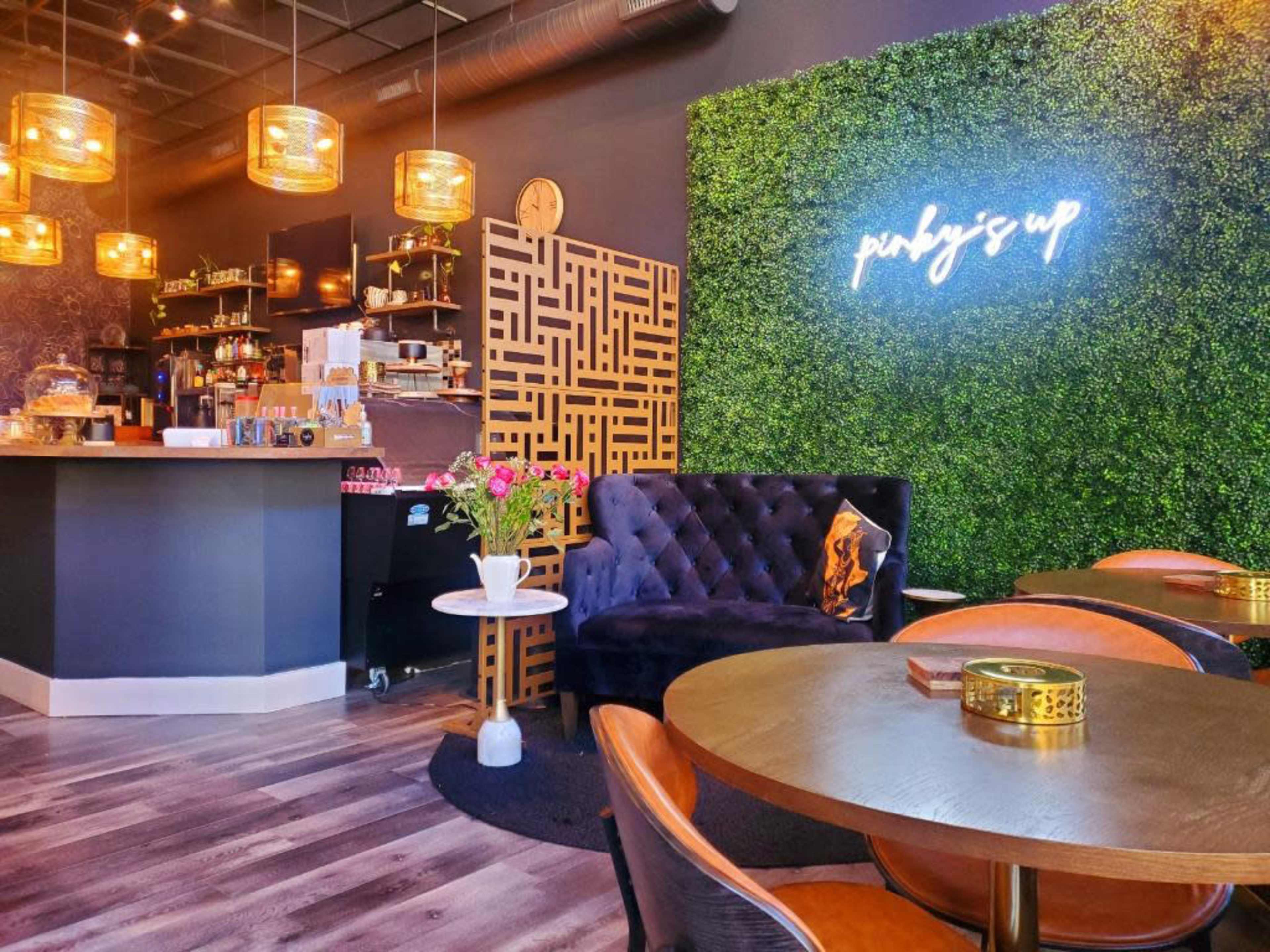 A modern café interior with a green wall feature, a bar area stocked with various items, and a cozy seating arrangement.