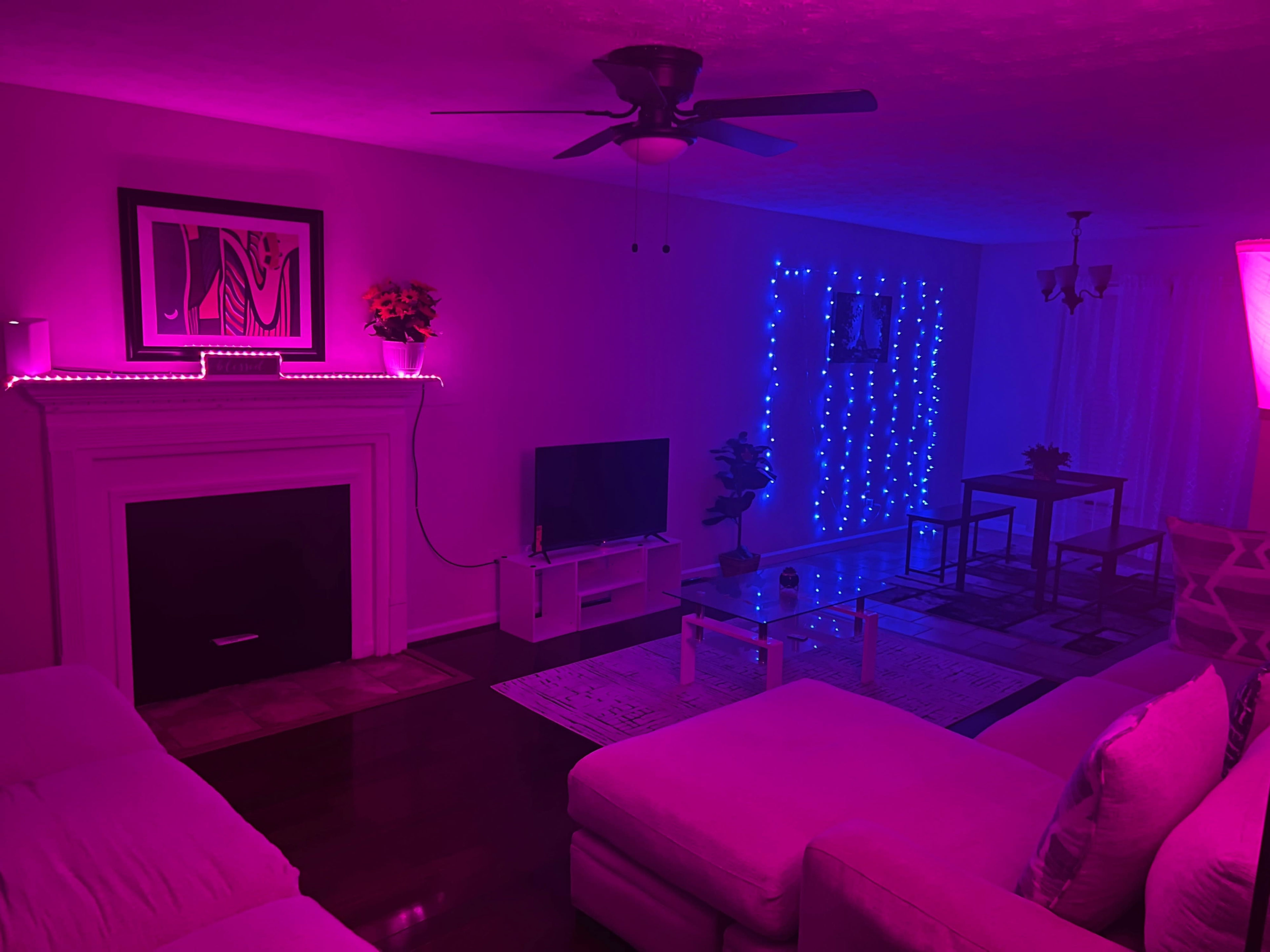 A modern living room with purple and blue LED lighting, featuring a sofa, television, coffee table, and dining area.