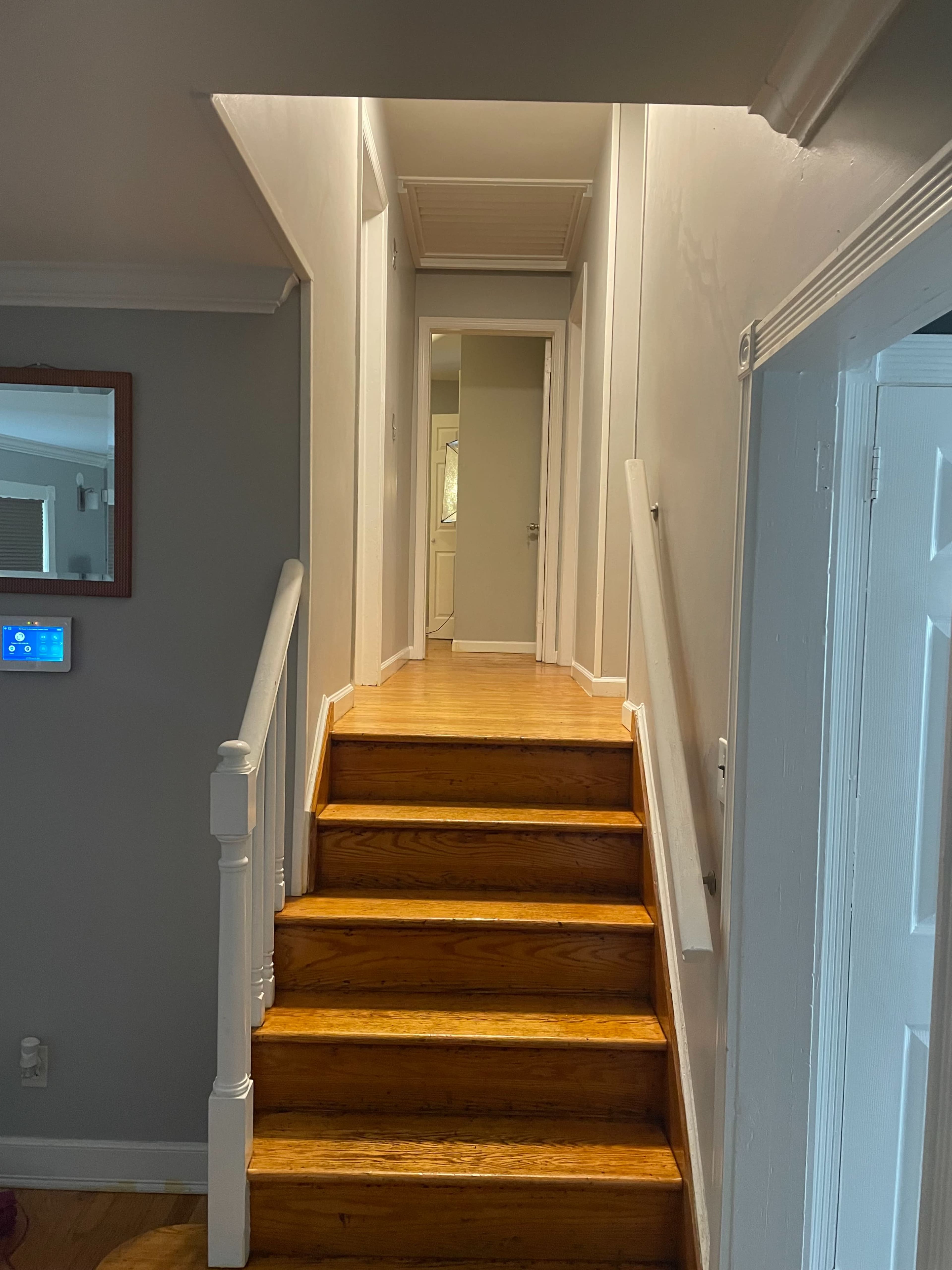 The image shows a hardwood staircase leading to a hallway with white walls and a closed door at the top.