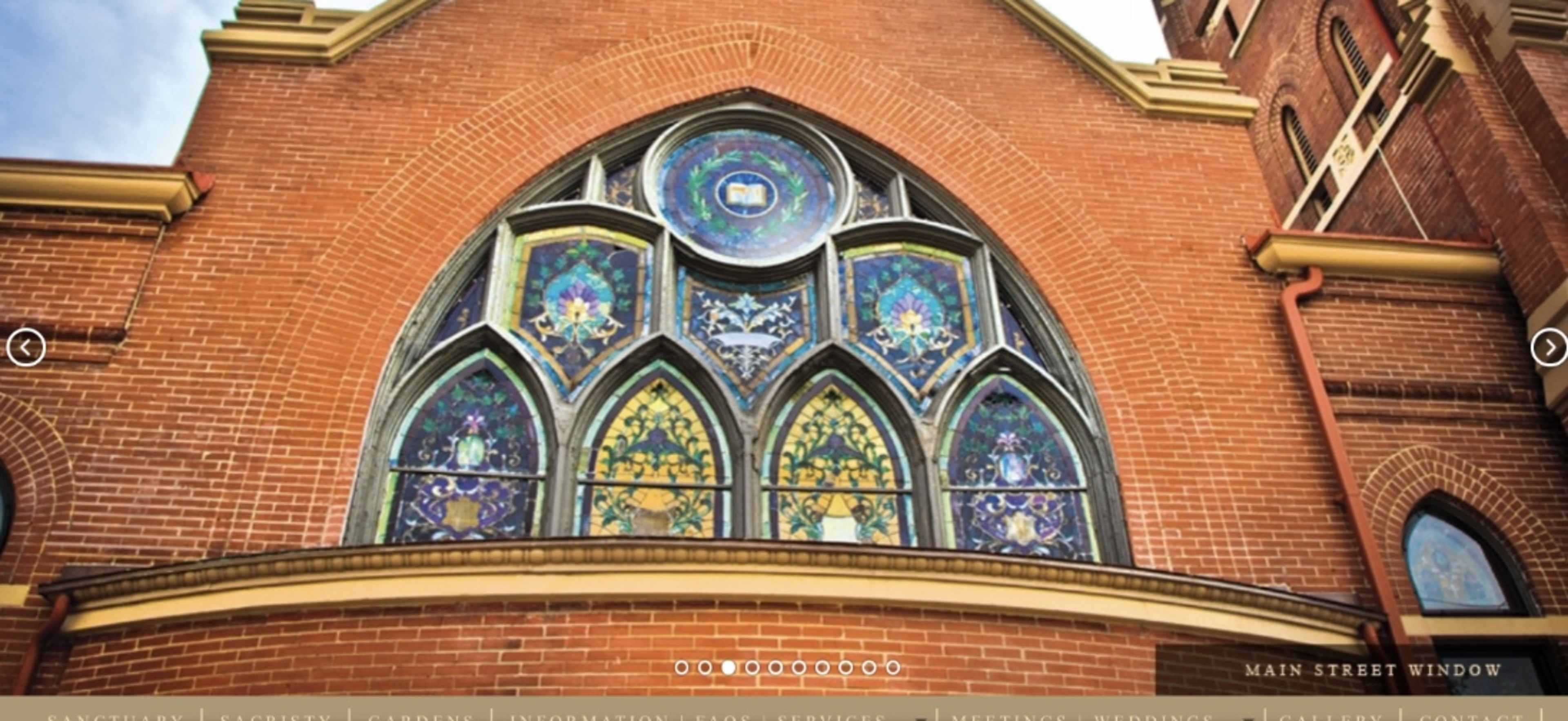 A large, ornate stained glass window set in a brick wall of a building.