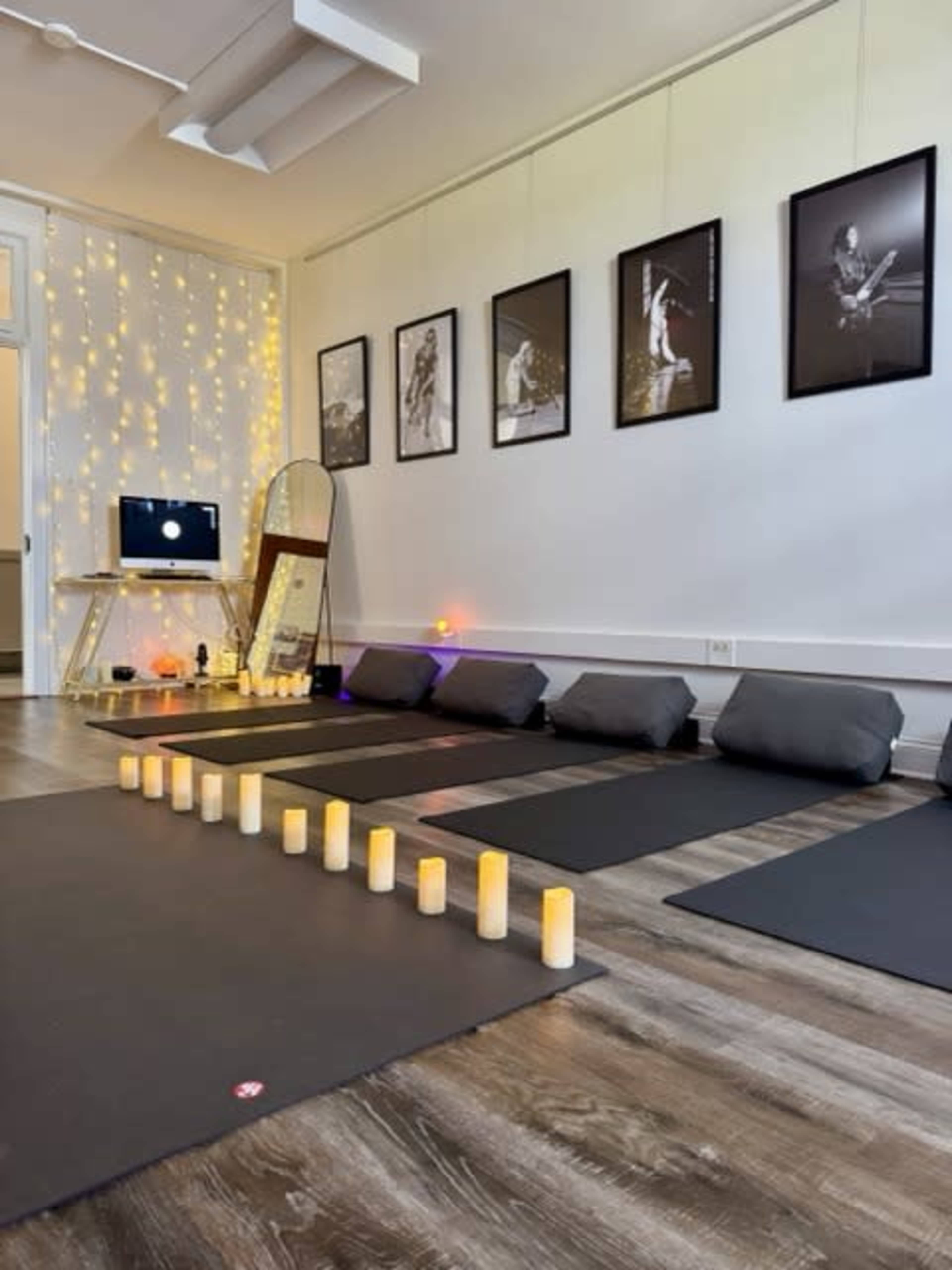 The room features several yoga mats arranged on the floor, with decorative candles lined up in front, framed photographs hanging on the wall, and ambient lighting creating a tranquil atmosphere.