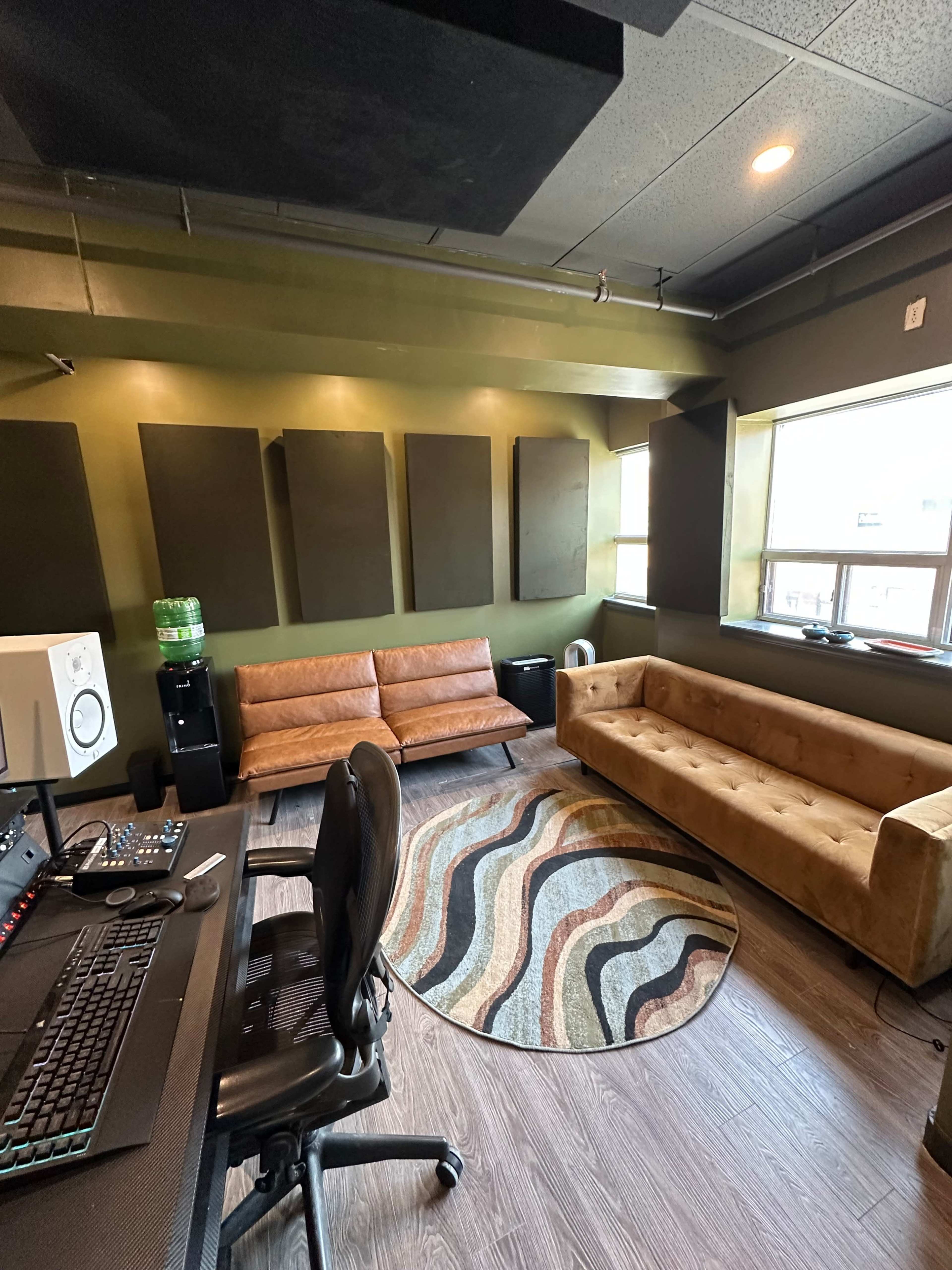 The image shows a music studio featuring two sofas, sound-absorption panels on the walls, and a desk with audio equipment.