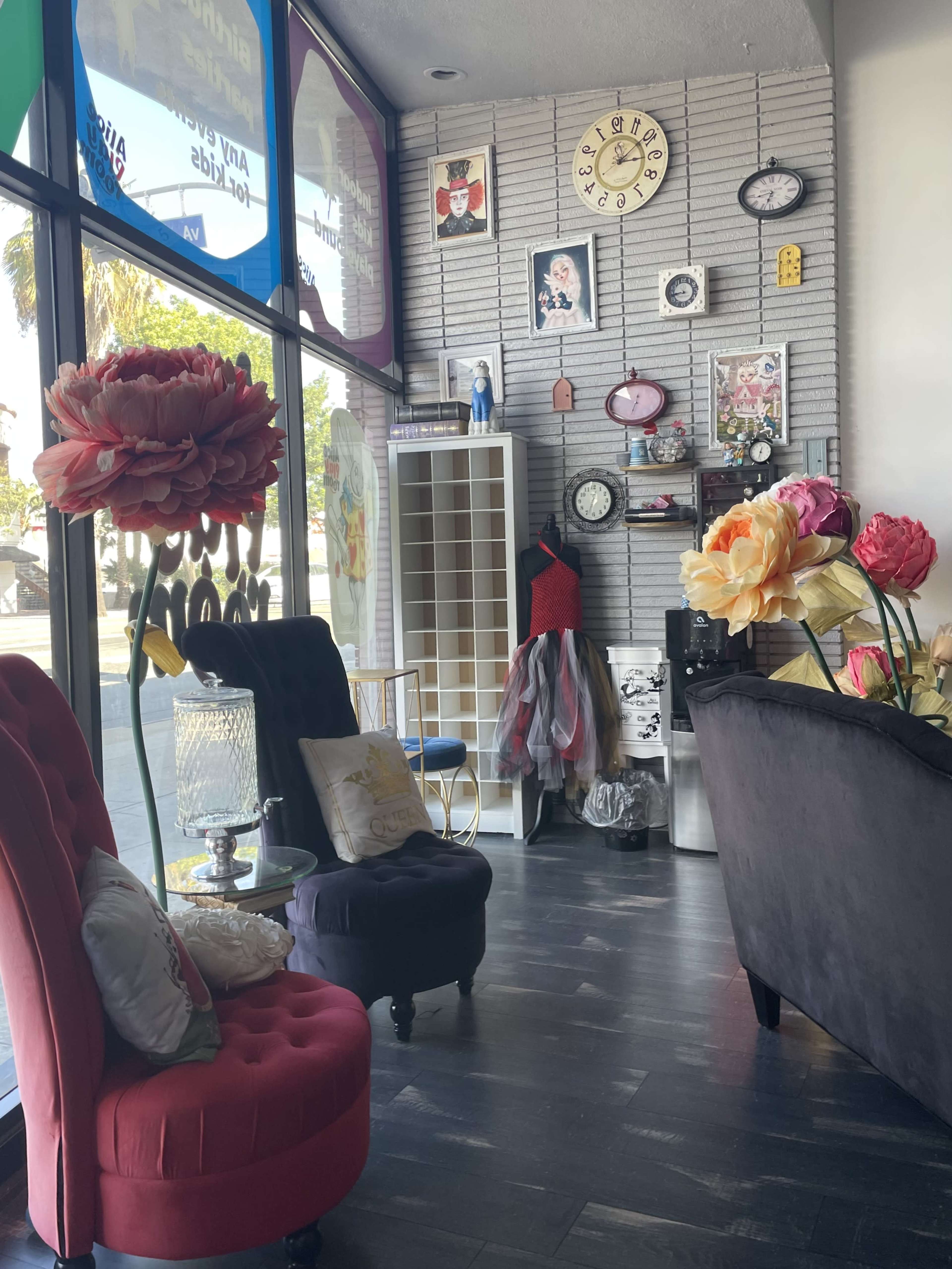 The image shows a retail space with colorful decorations, including oversized flowers, vintage clocks, and a display of various clothing items against a brick wall.