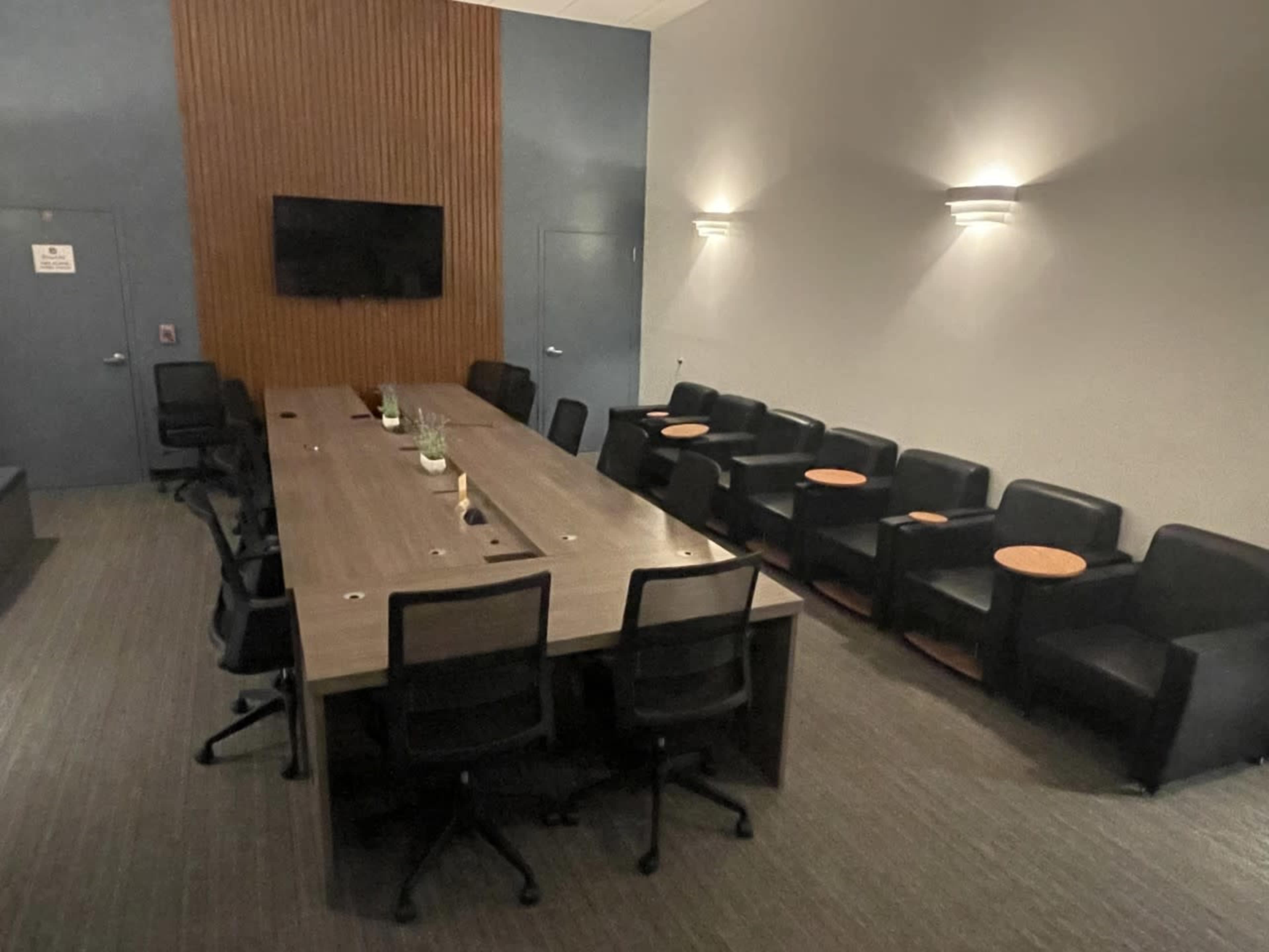 A conference room features a long table with seating and a wall-mounted screen, illuminated by wall sconces.