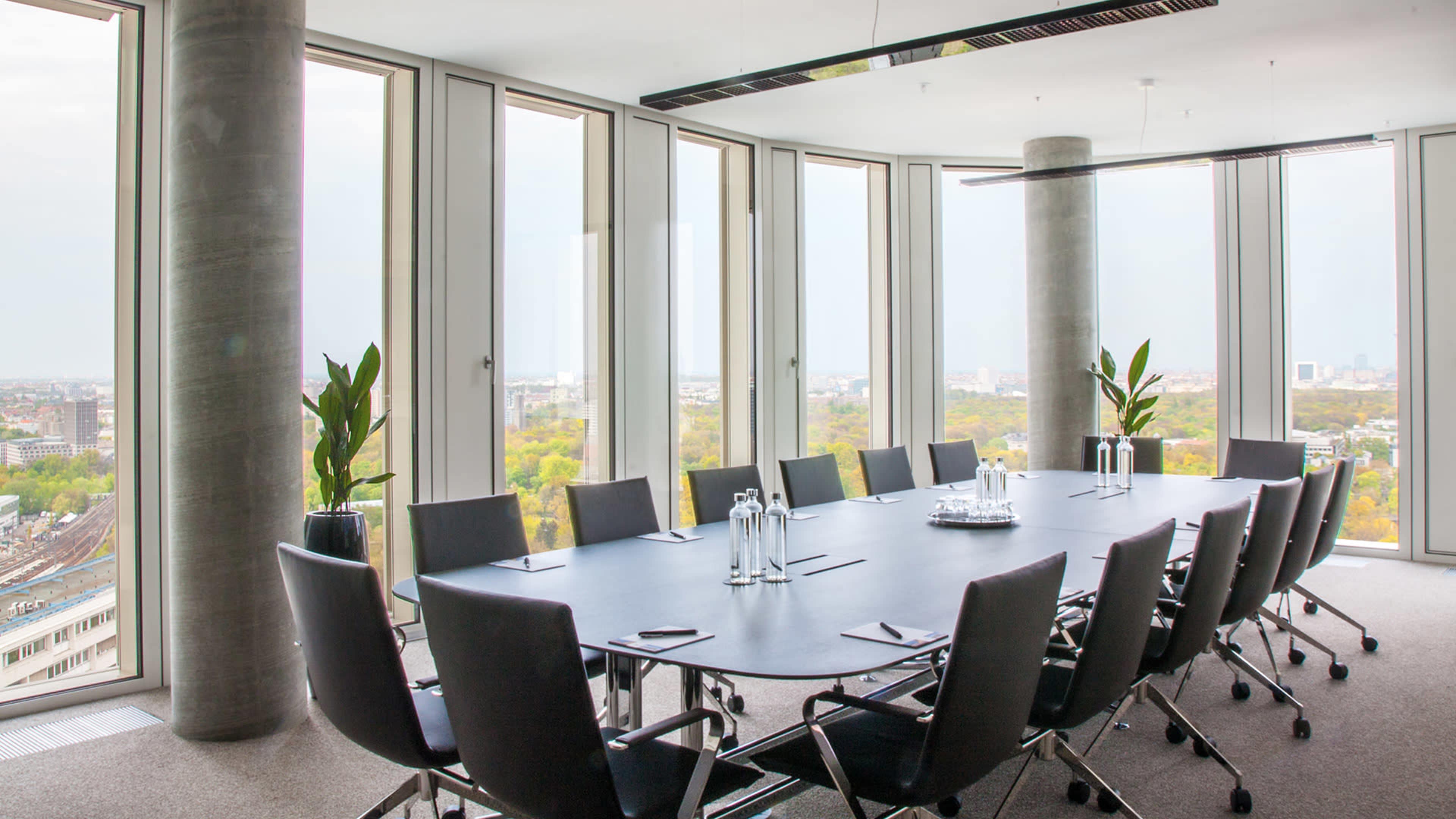 A modern conference room features a long black table surrounded by ergonomic chairs, with large windows offering a panoramic view of the city.