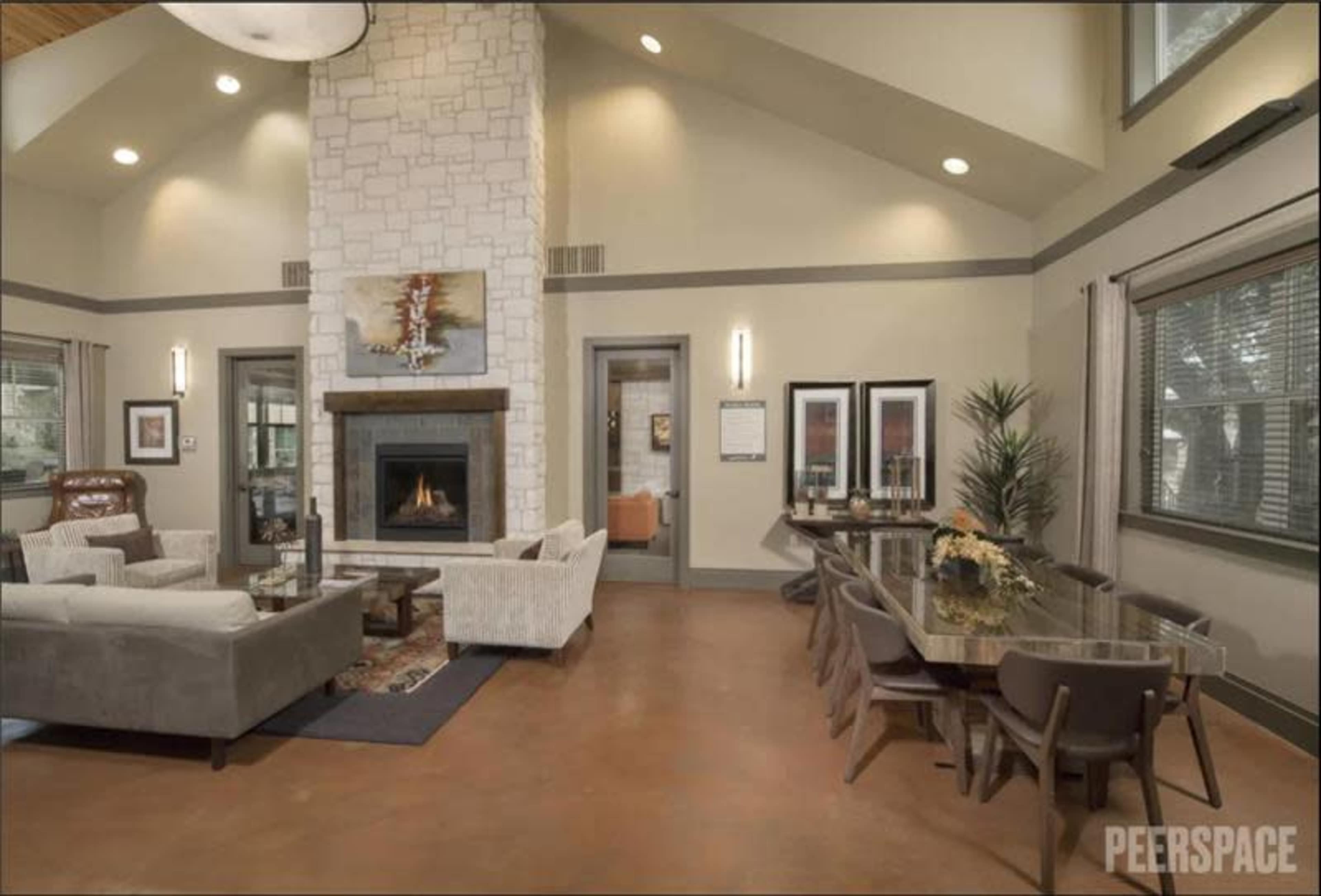 The image shows a spacious, modern living room with a stone fireplace, comfortable seating, and a dining area featuring a glass table.