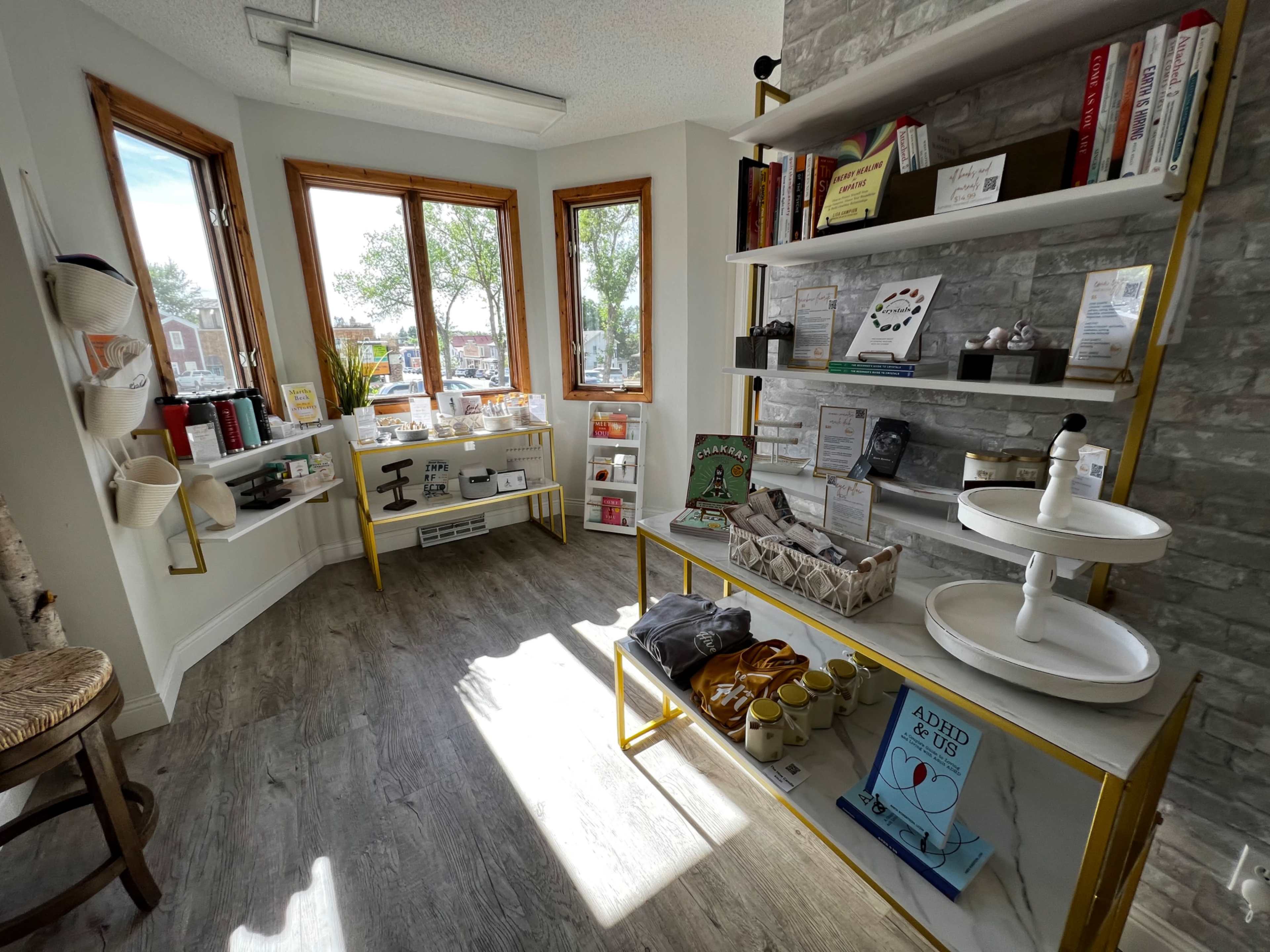 A bright interior of a boutique with wooden shelves displaying various products and a corner window allowing natural light to enter.