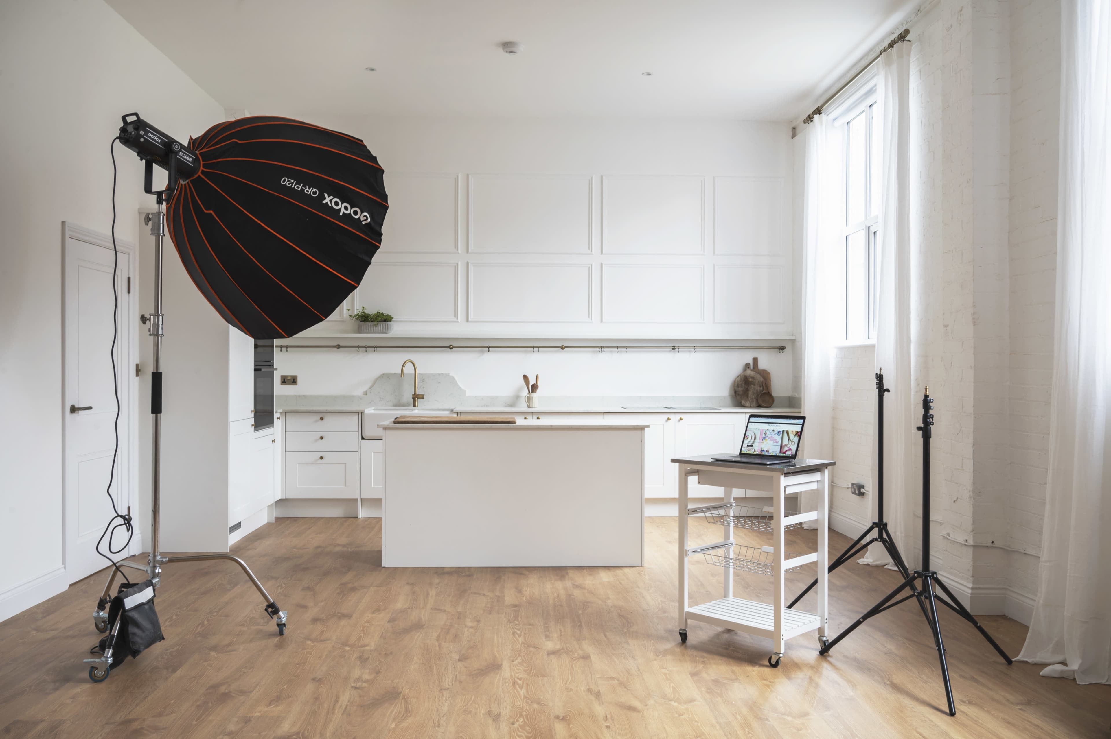 A modern kitchen with white cabinetry, a central island, and a photography lighting setup on the side.