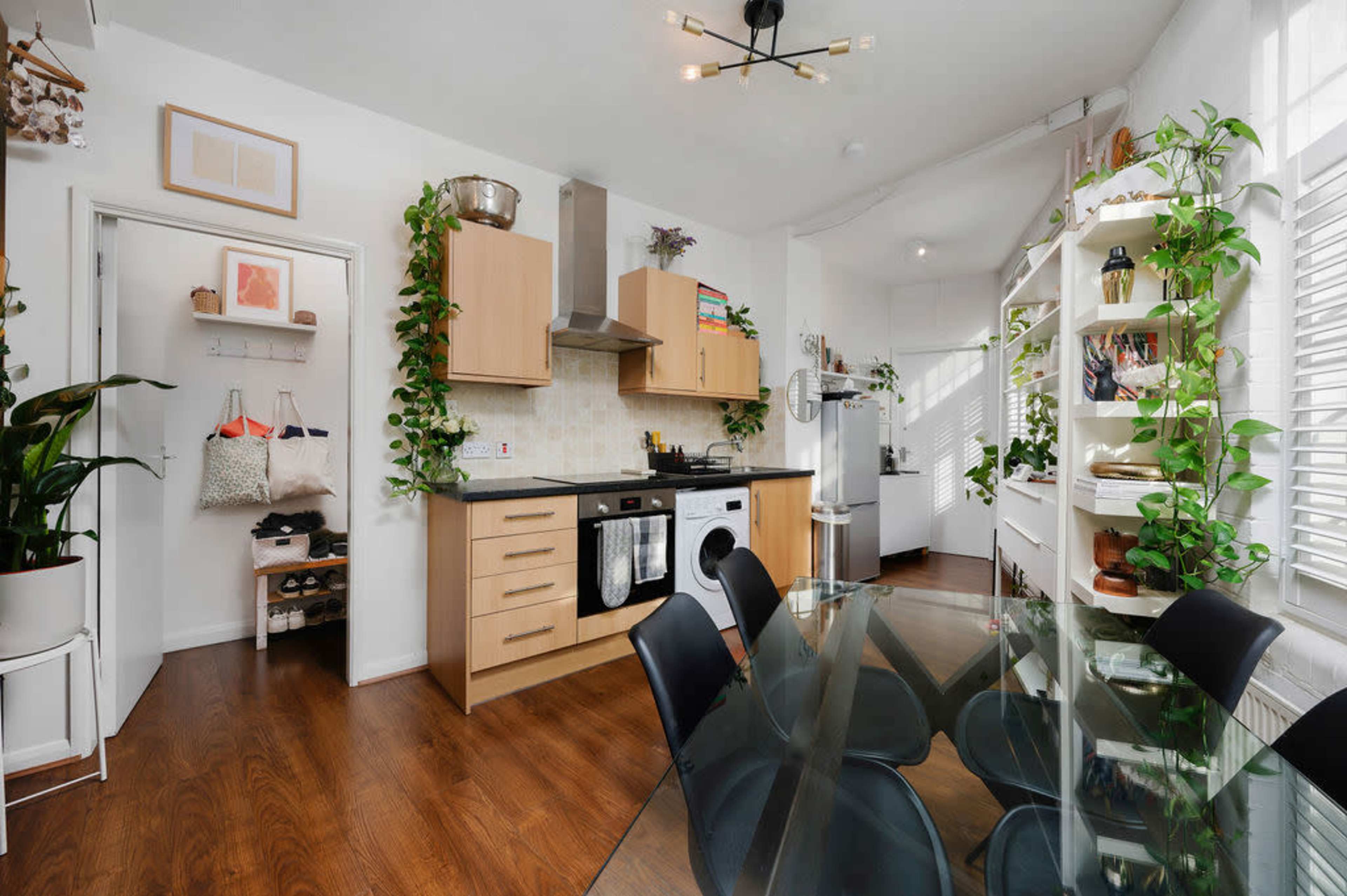 A modern kitchen and dining area feature wooden cabinetry, stainless steel appliances, and plants adorning the walls.