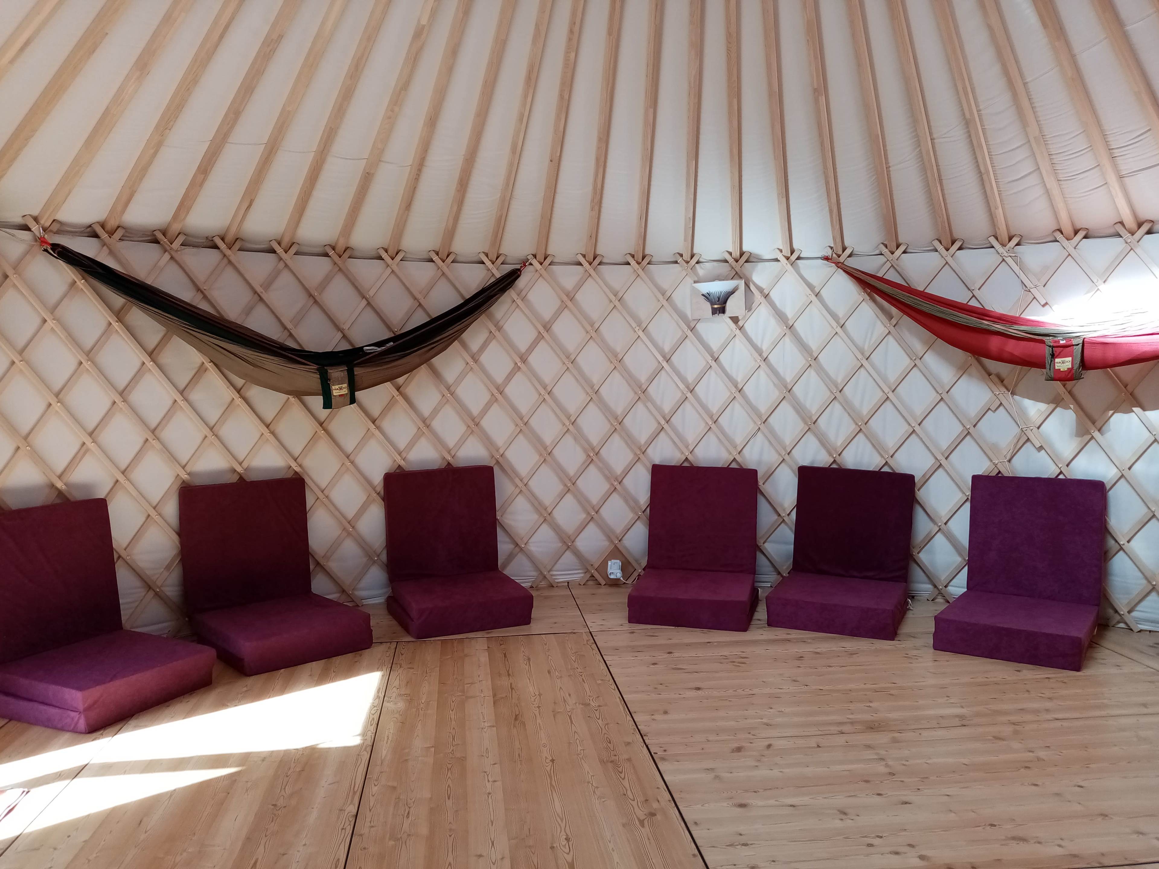 A circular yurt interior with six purple seated cushions arranged around the floor and two hammocks hanging from the walls.