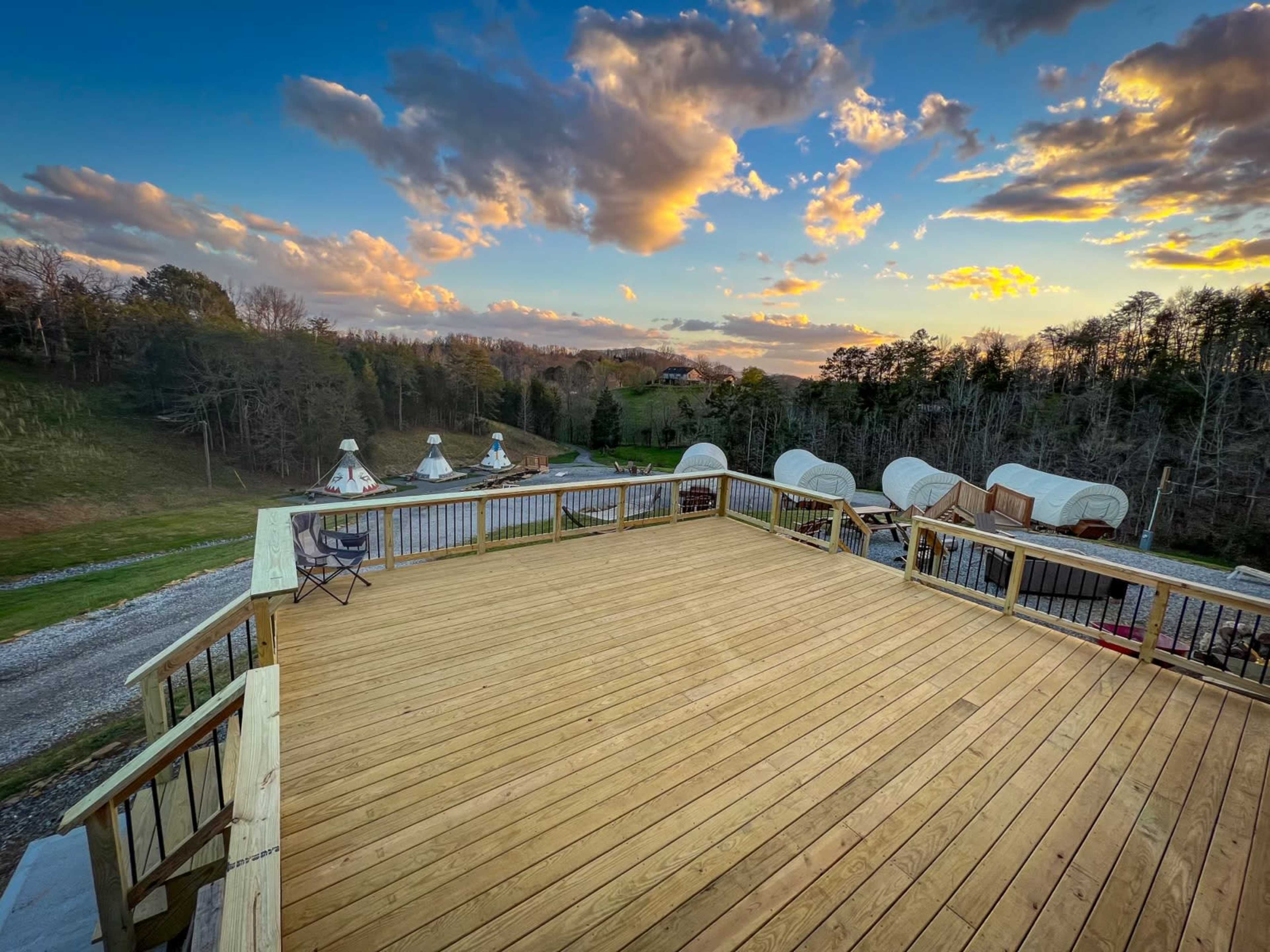 A wooden deck overlooks a tree-lined hillside under a colorful sunset sky.