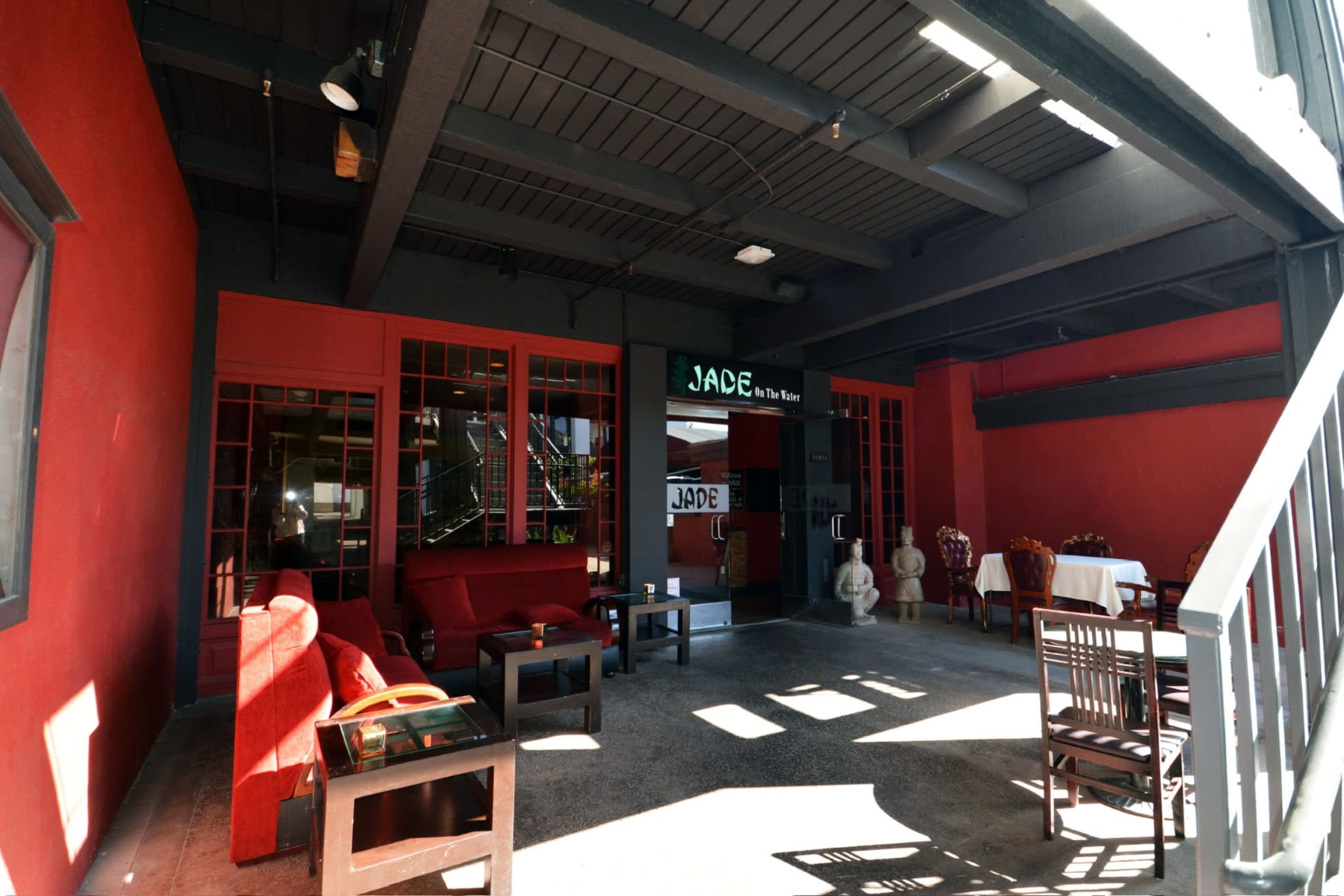 The image shows a well-furnished outdoor dining area with red walls, wooden furniture, and a restaurant entrance labeled "JADE."
