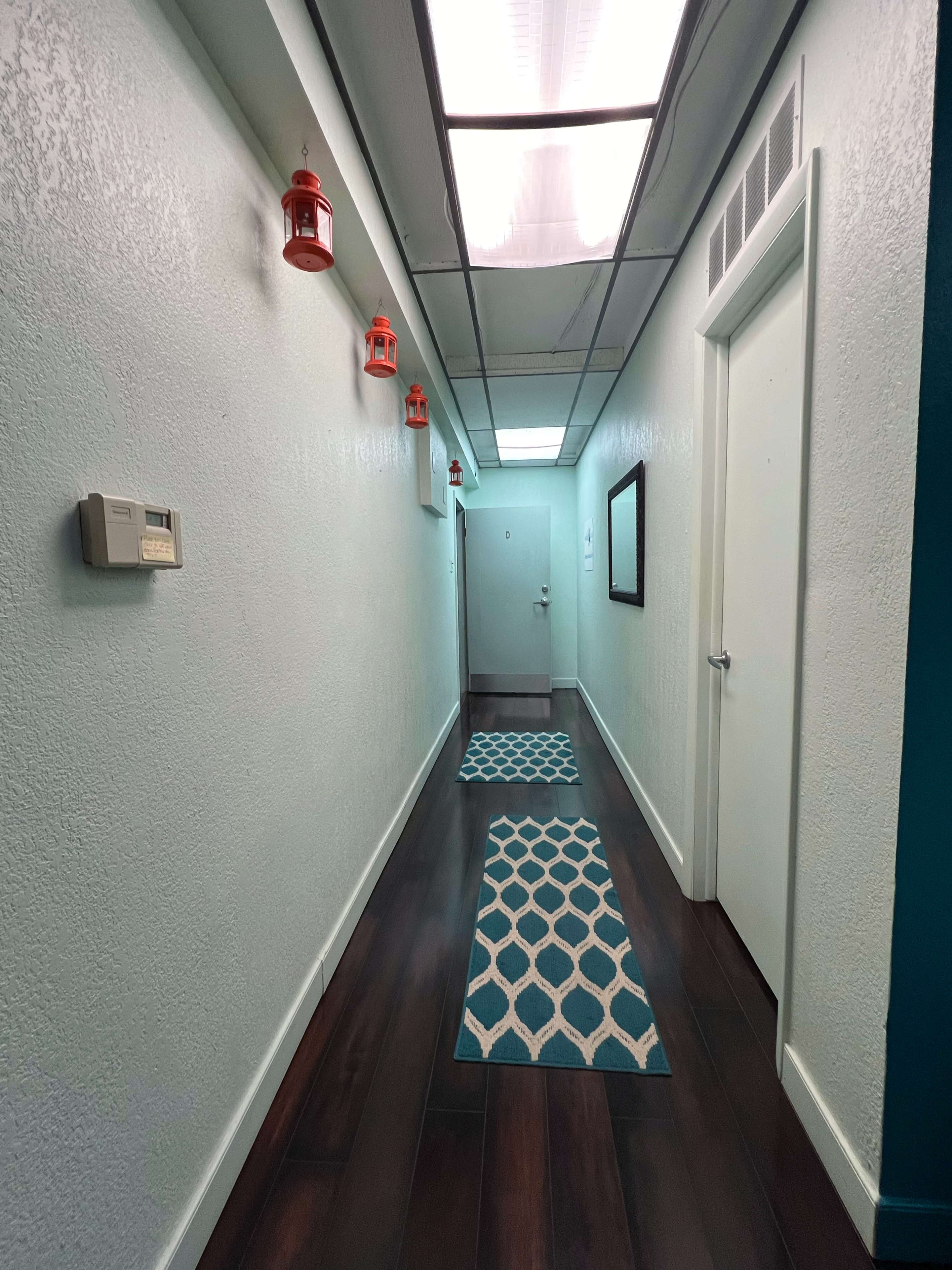 A long hallway features light blue walls, wooden flooring, decorative rugs, and red lanterns hanging from the ceiling.