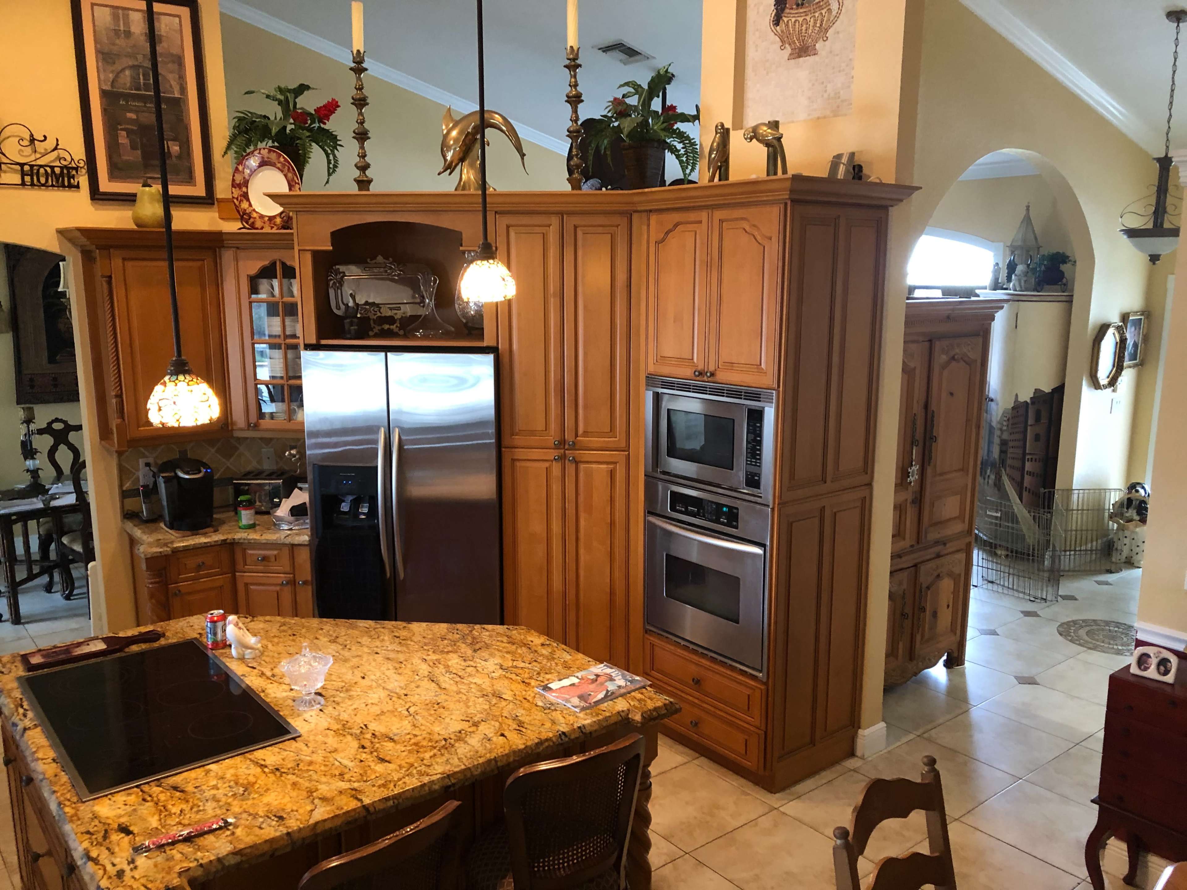 A spacious kitchen with wooden cabinetry, stainless steel appliances, and a countertop made of granite, adjoining a dining area and a hallway leading to another room.