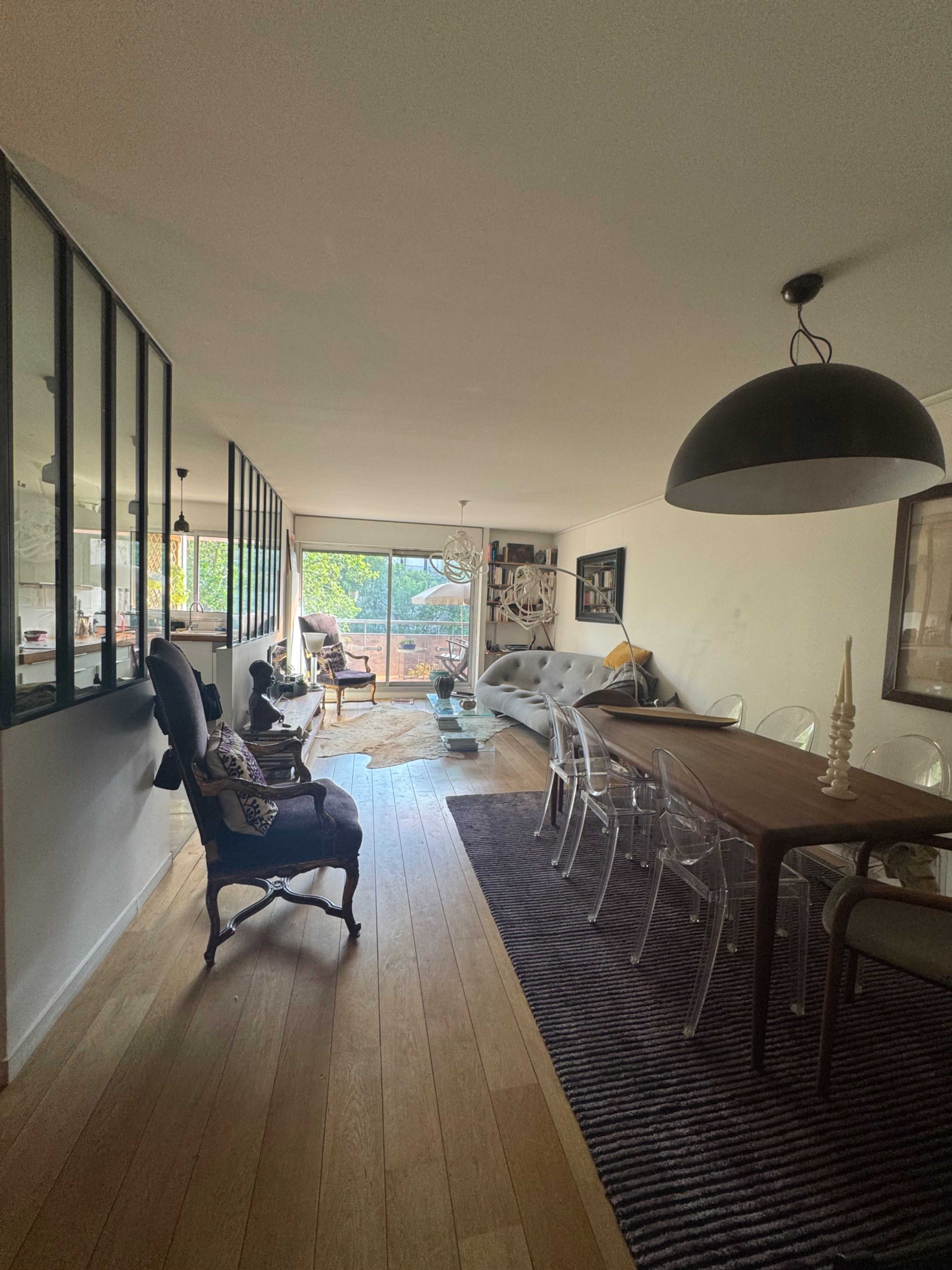 The image shows a modern open-concept living and dining area with large windows, hardwood flooring, and a mix of contemporary and classic furniture.