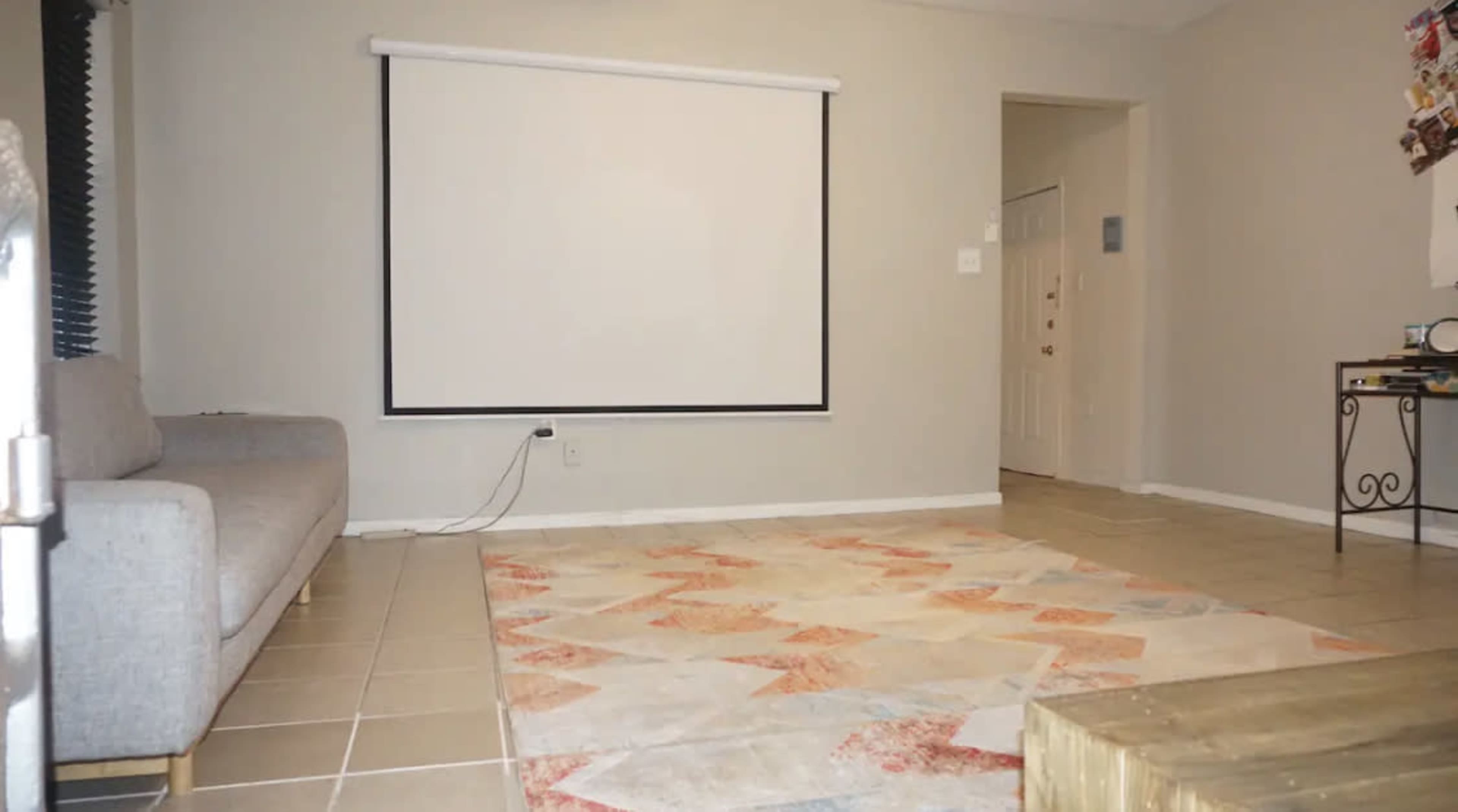A living room with a gray sofa, a large area rug, and a retractable projection screen mounted on the wall.