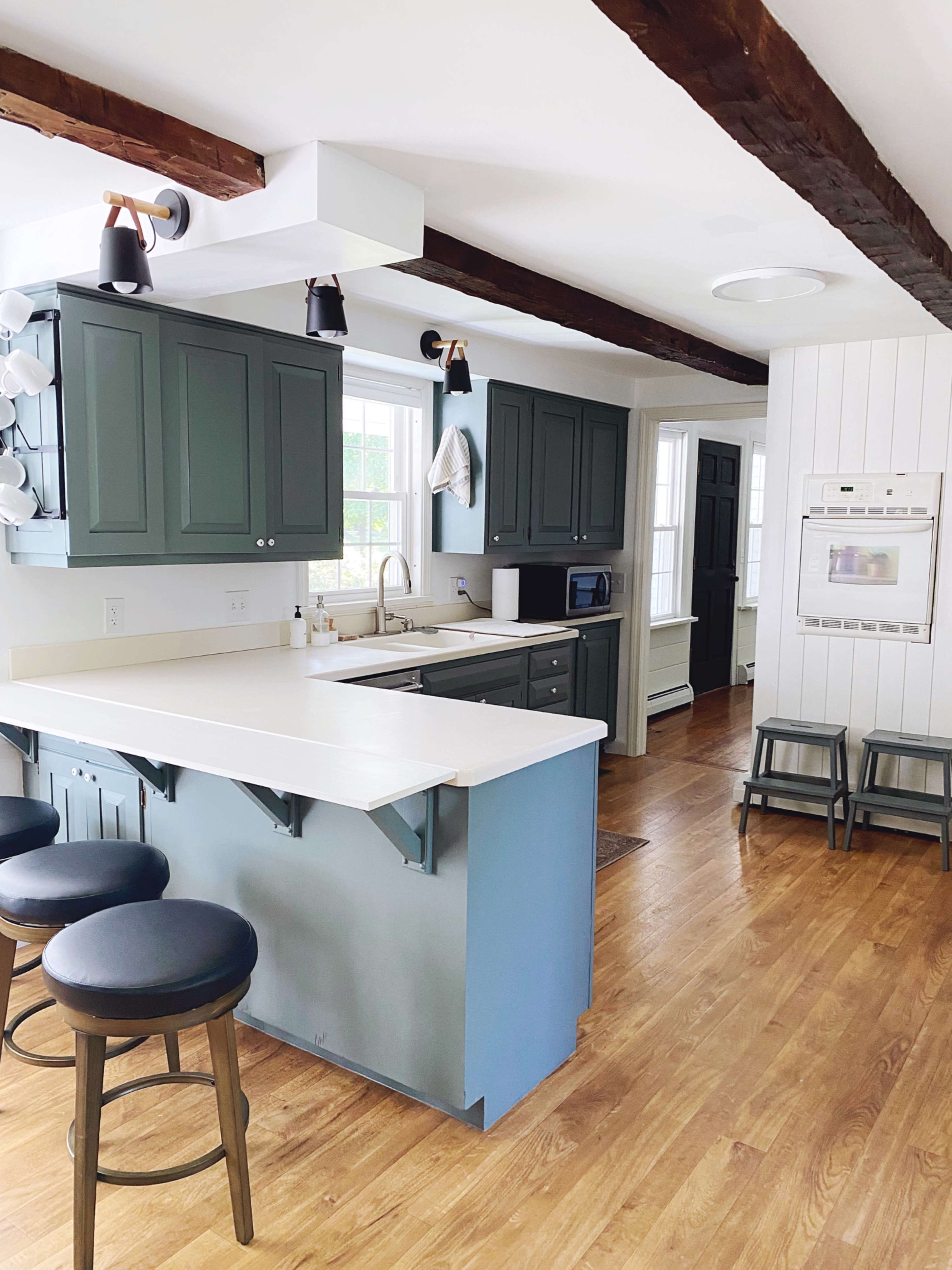 A modern kitchen with green cabinetry, a light-colored countertop, and a mix of wood and white accents.
