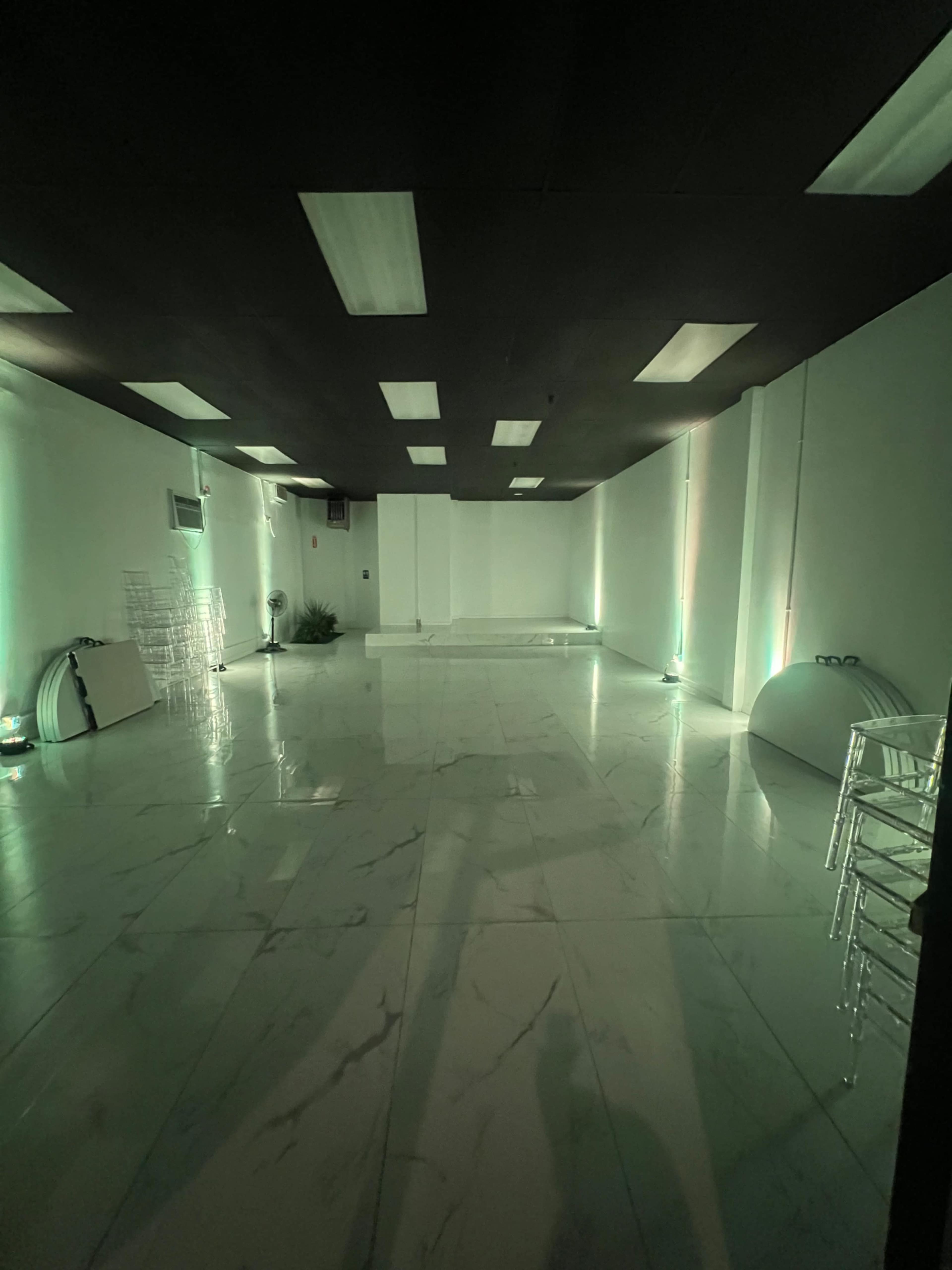 A spacious, empty room with marble flooring and green lighting along the walls.