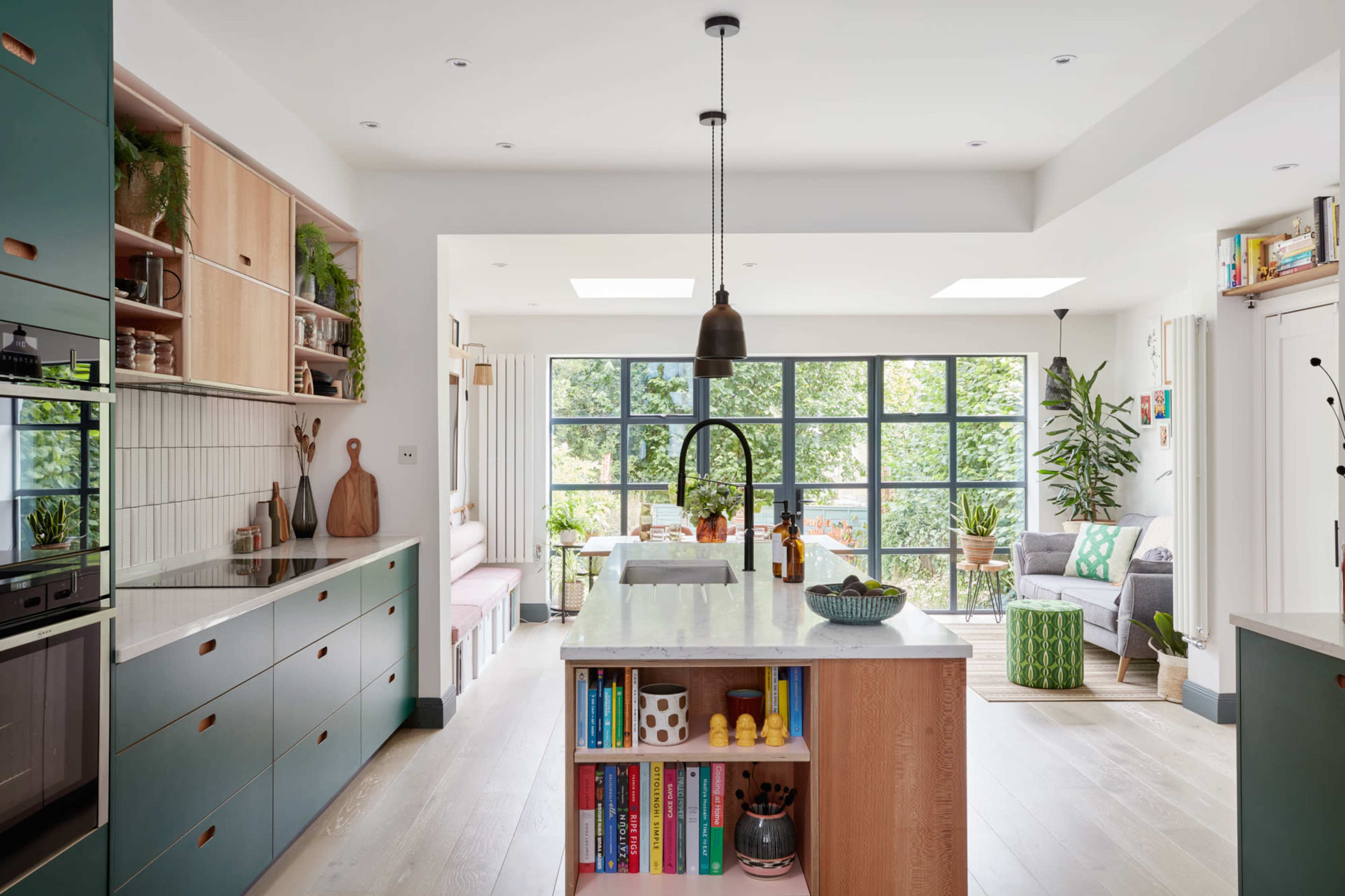 A modern kitchen features green cabinetry, a central island with a marble countertop, and large windows allowing natural light to illuminate the space.