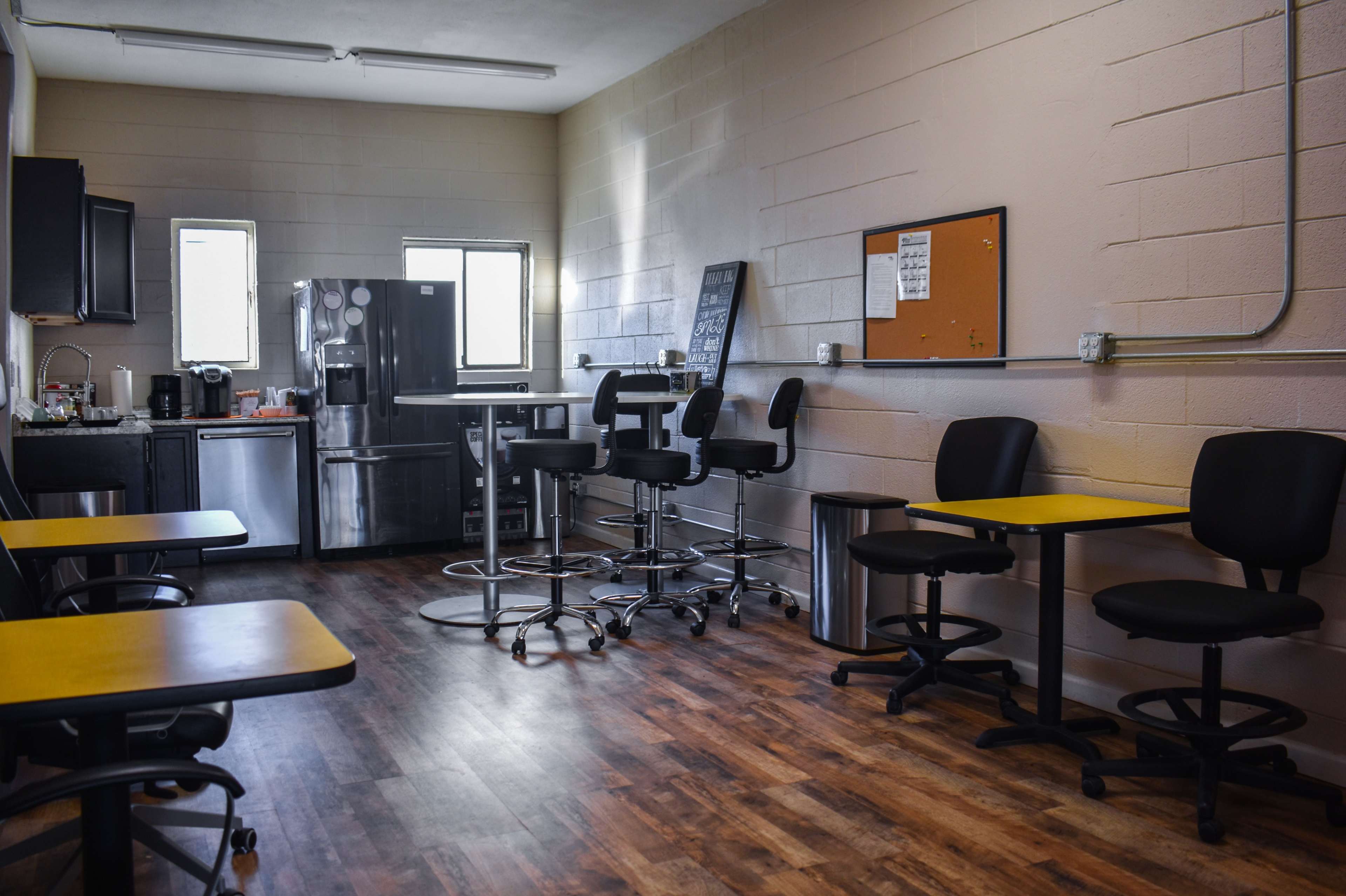 A break room with black chairs and tables, a refrigerator, and a kitchenette area along one wall.