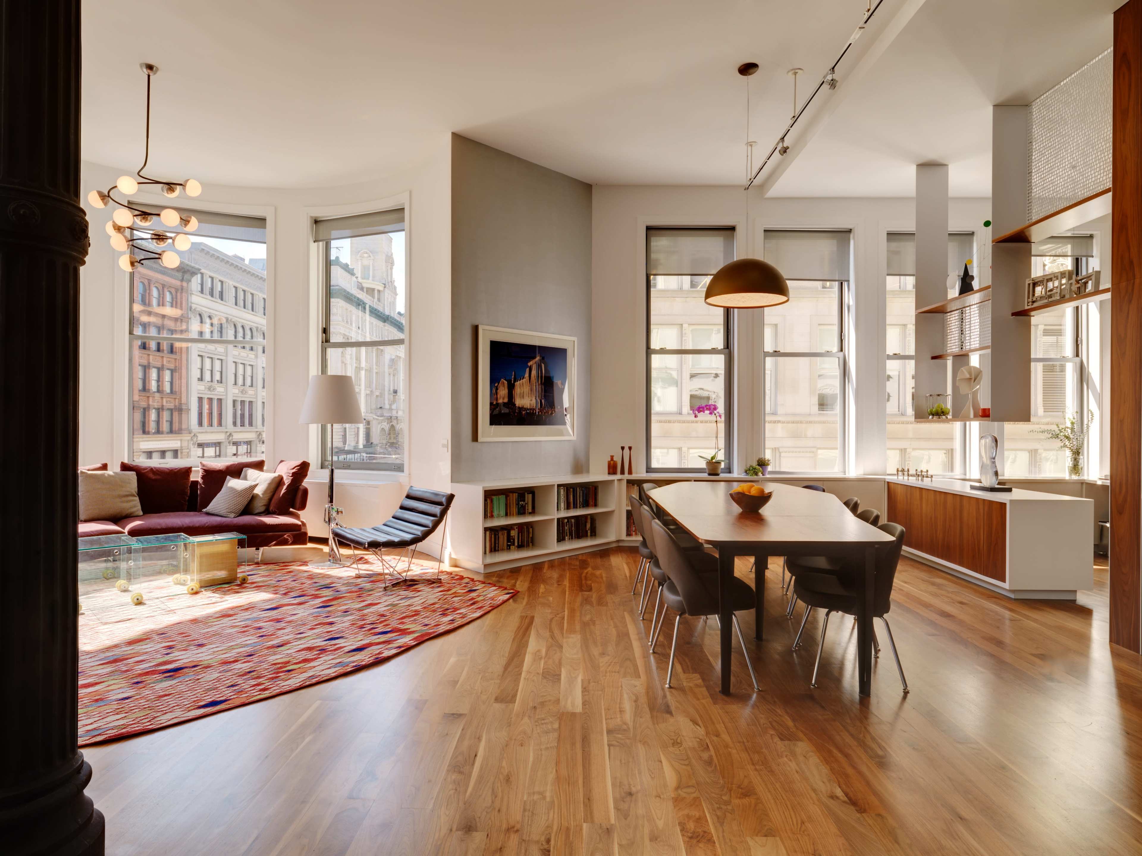 The image shows a modern, open-concept living space featuring a cozy seating area with large windows, a dining table, and wooden flooring.