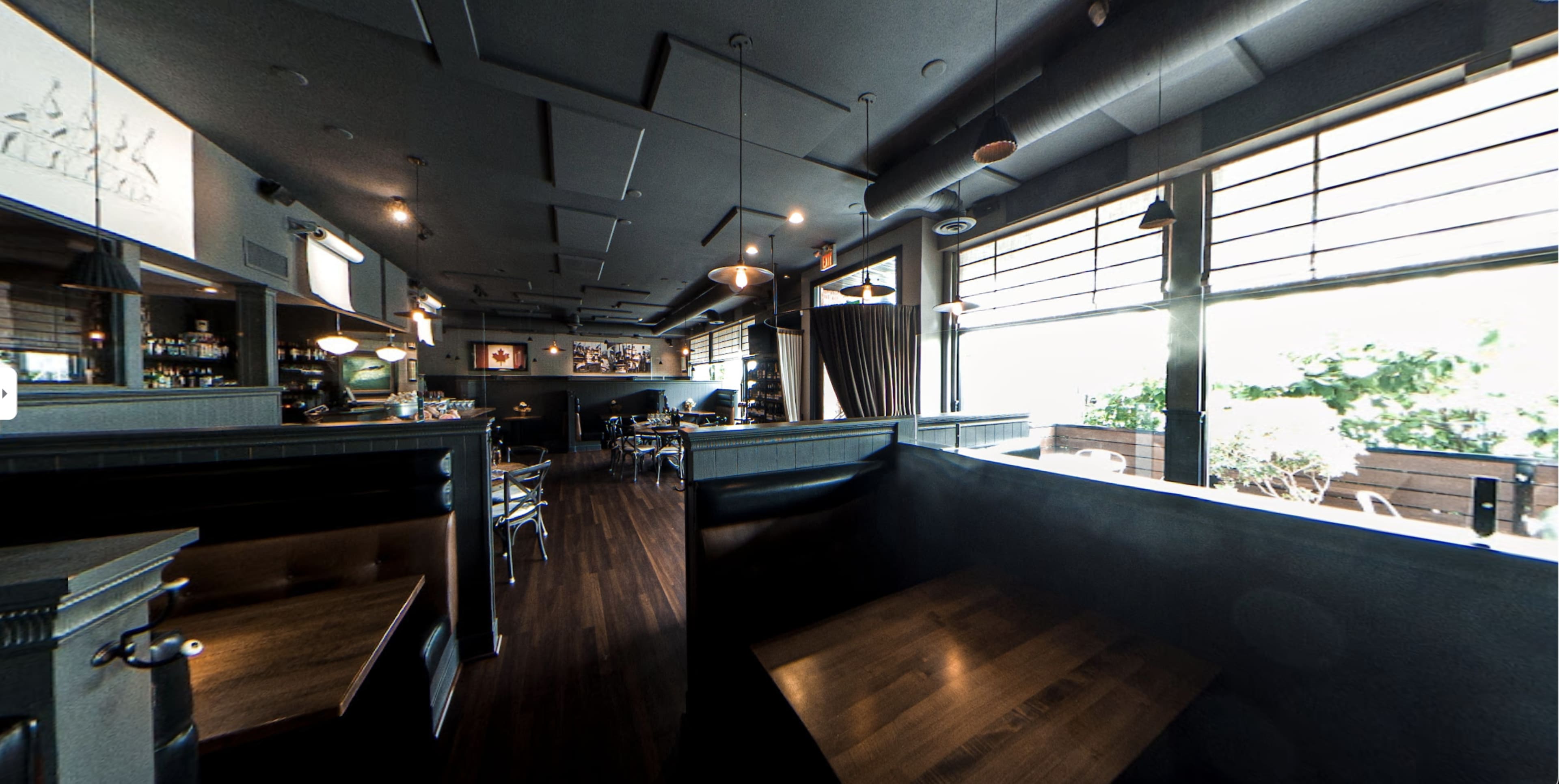 A modern restaurant interior with wooden tables, a bar area, and large windows allowing natural light to enter.