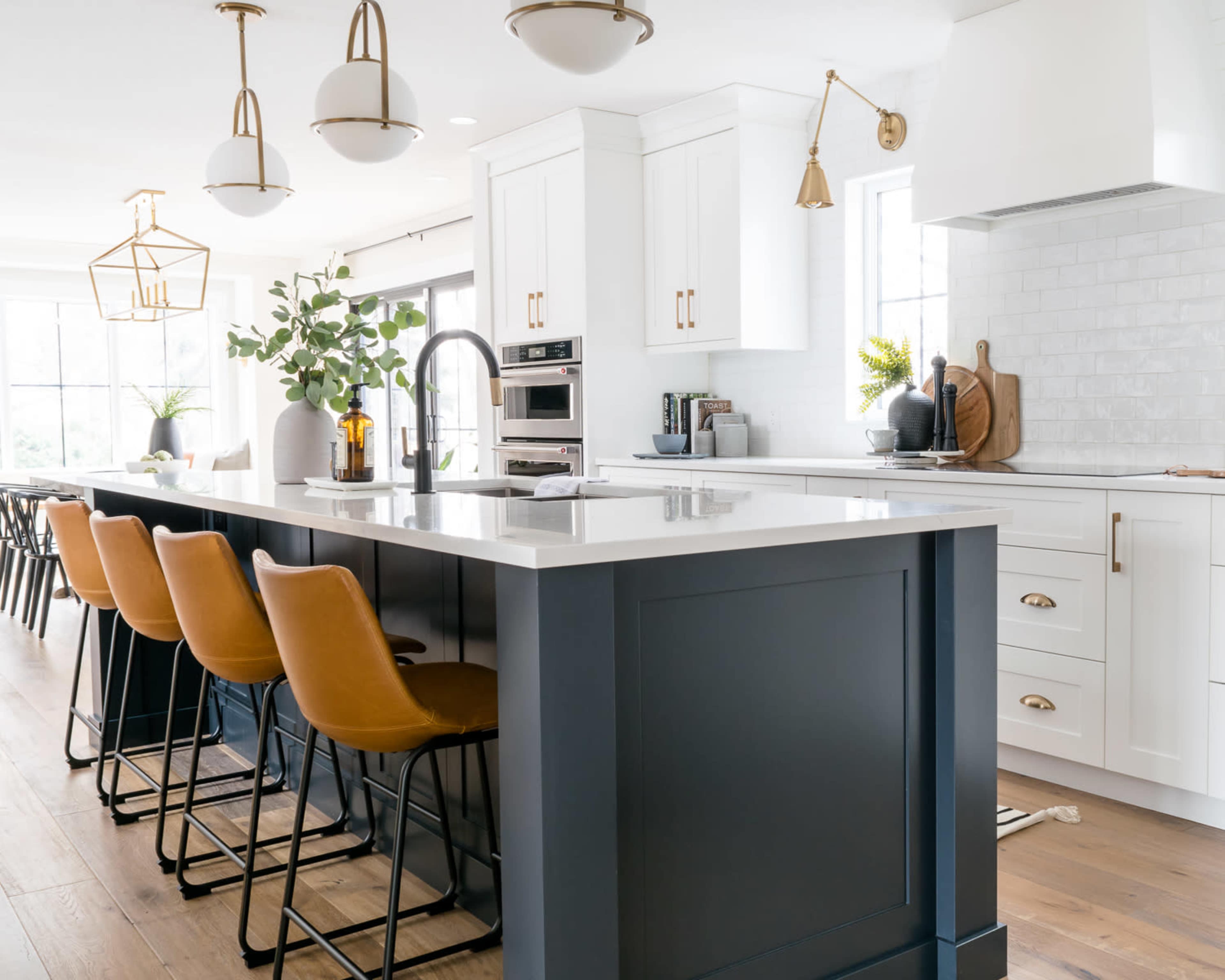 A modern kitchen features white cabinetry, a large island with seating, stainless steel appliances, and decorative light fixtures.