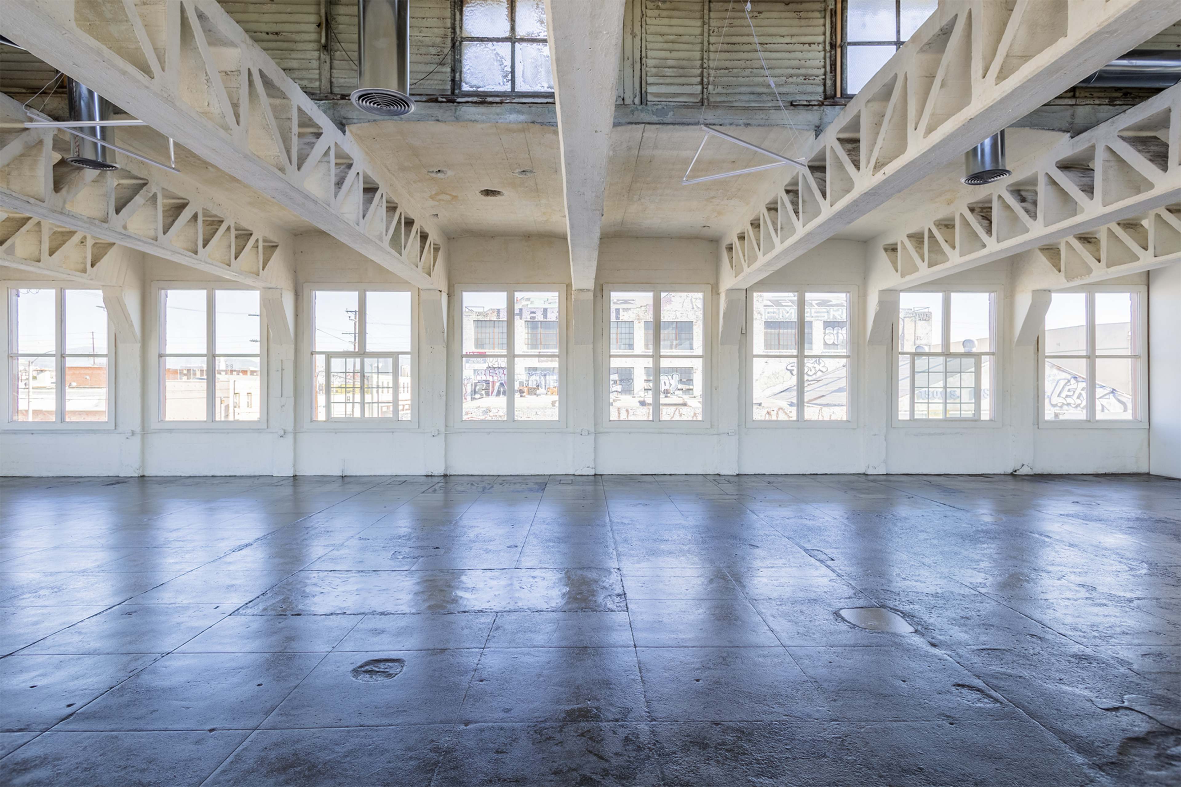 An empty industrial space features large, rectangular windows along the walls, allowing natural light to flood in.