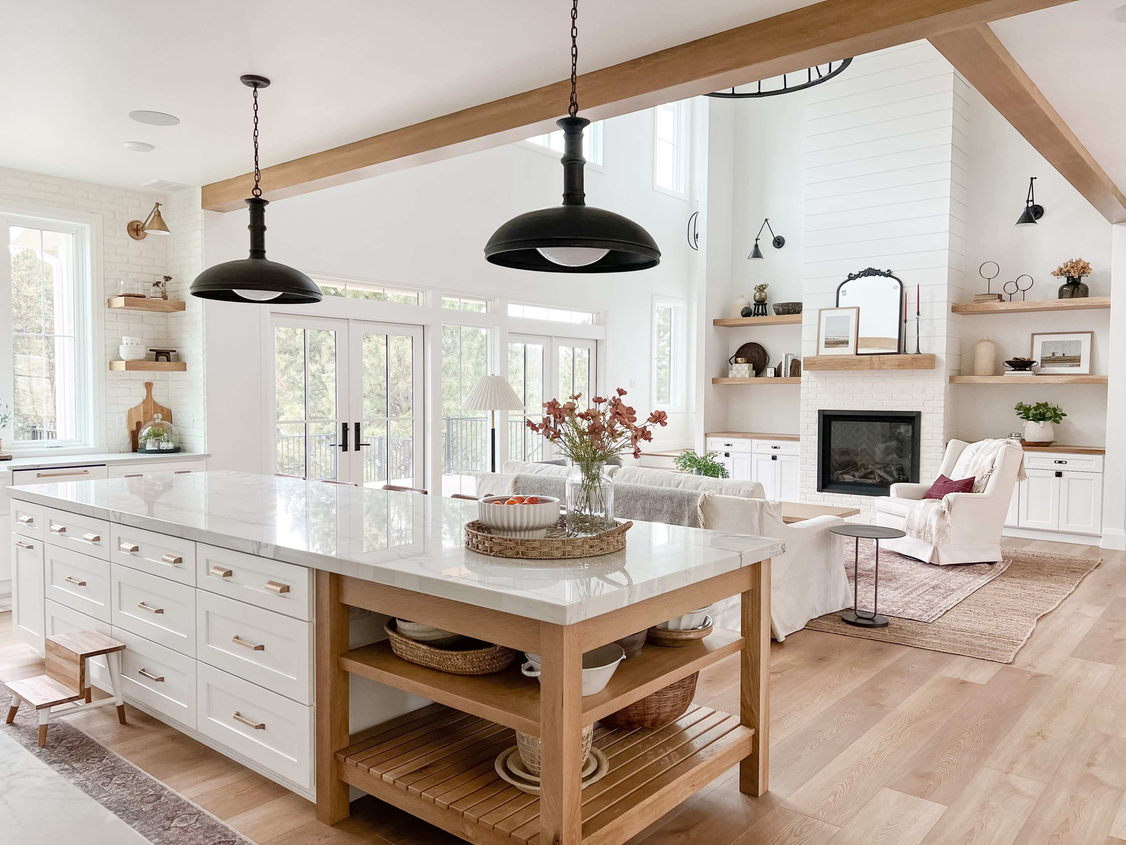 A bright, modern kitchen features a large island with white cabinetry and wooden accents, complemented by a cozy seating area with a fireplace and decorative shelves.