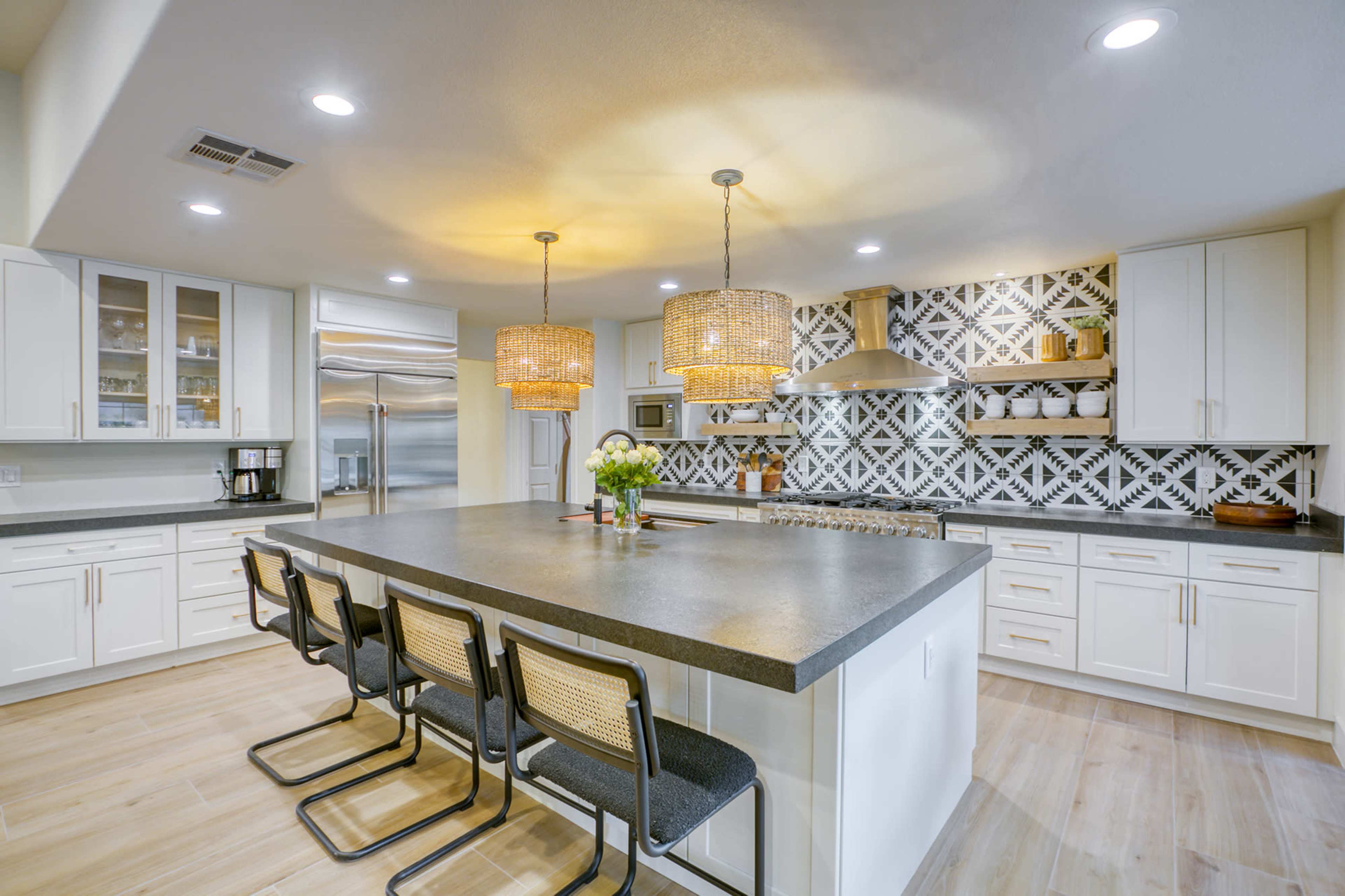 A modern kitchen features a large island with seating, decorative tile backsplash, and pendant lighting over the countertop.
