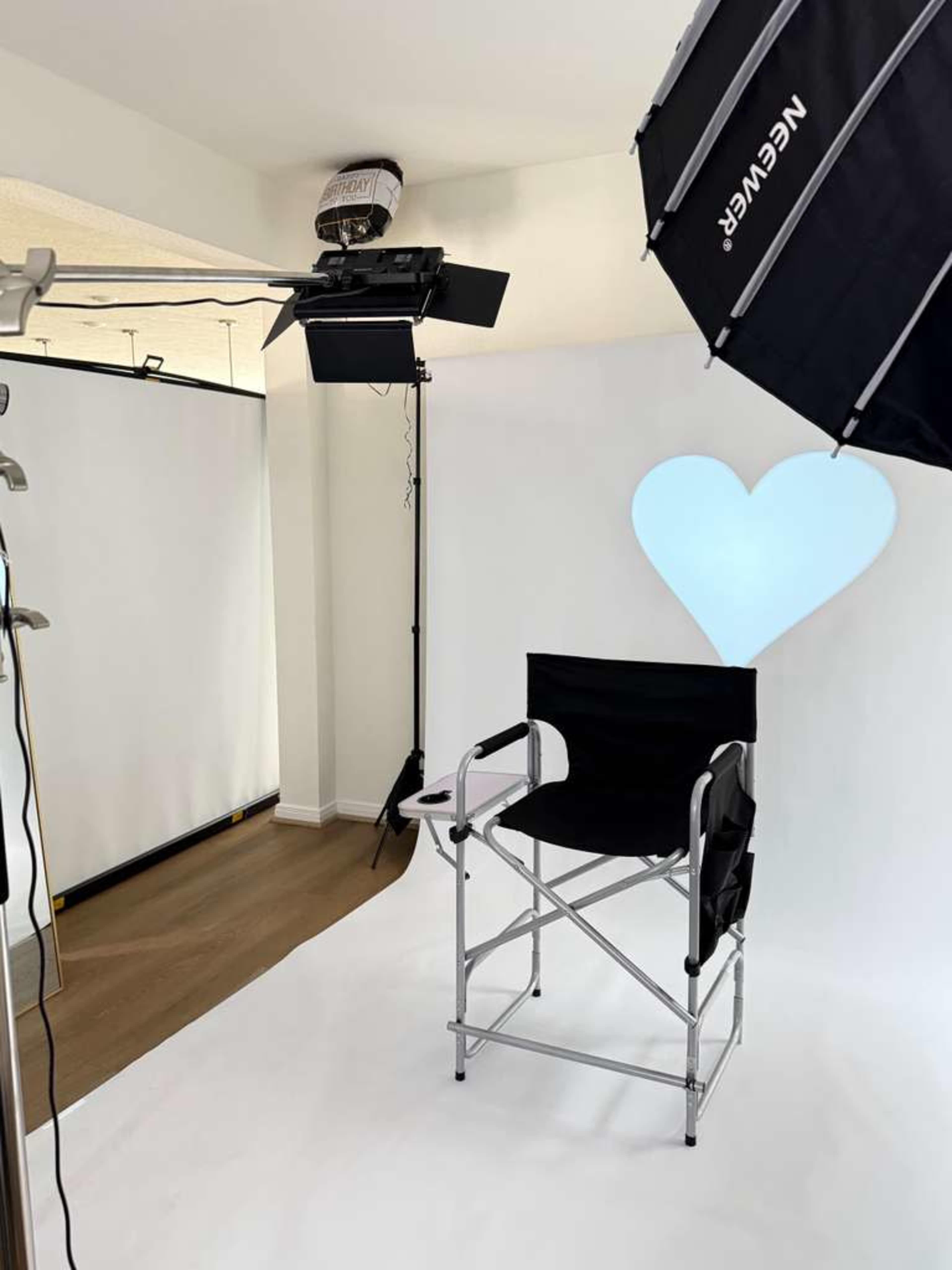 The image shows a photography studio setup featuring a black director's chair, a heart-shaped backdrop light, and various lighting equipment against a white background.
