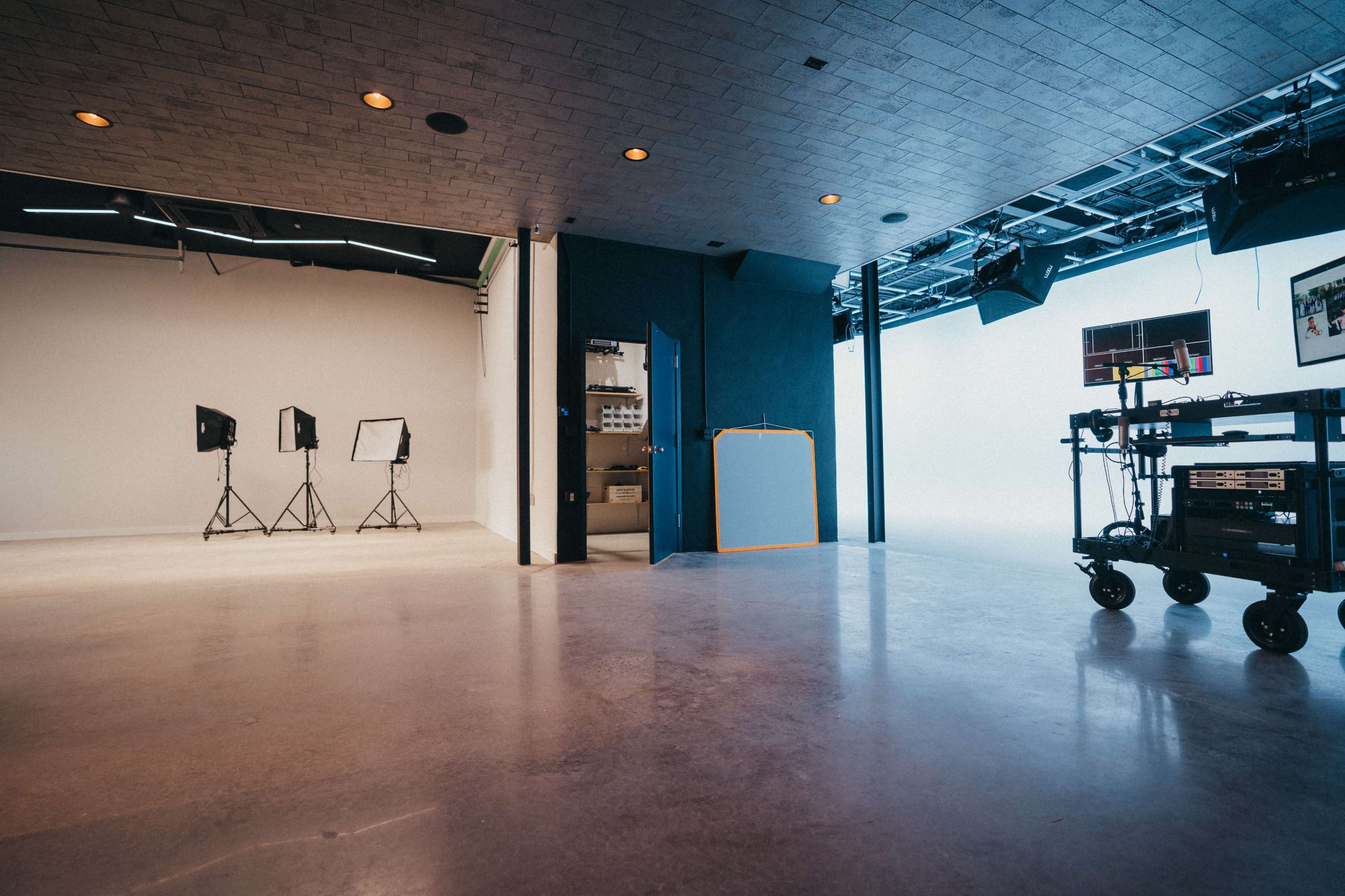A spacious photography studio with an empty backdrop, three light stands, and a equipment cart on wheels.
