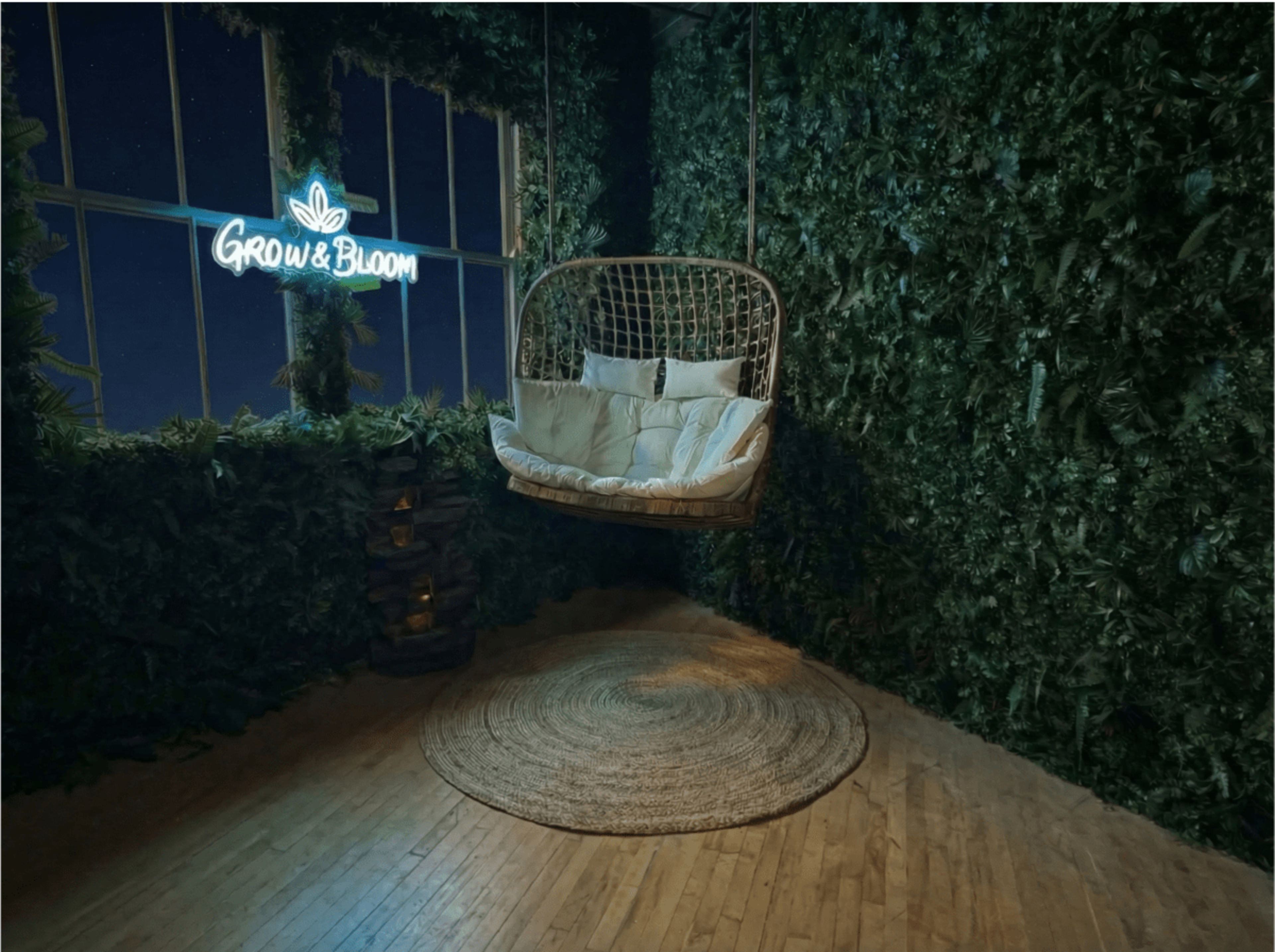 A hanging chair is suspended in a room adorned with greenery, featuring a neon sign that reads "Grow & Bloom."