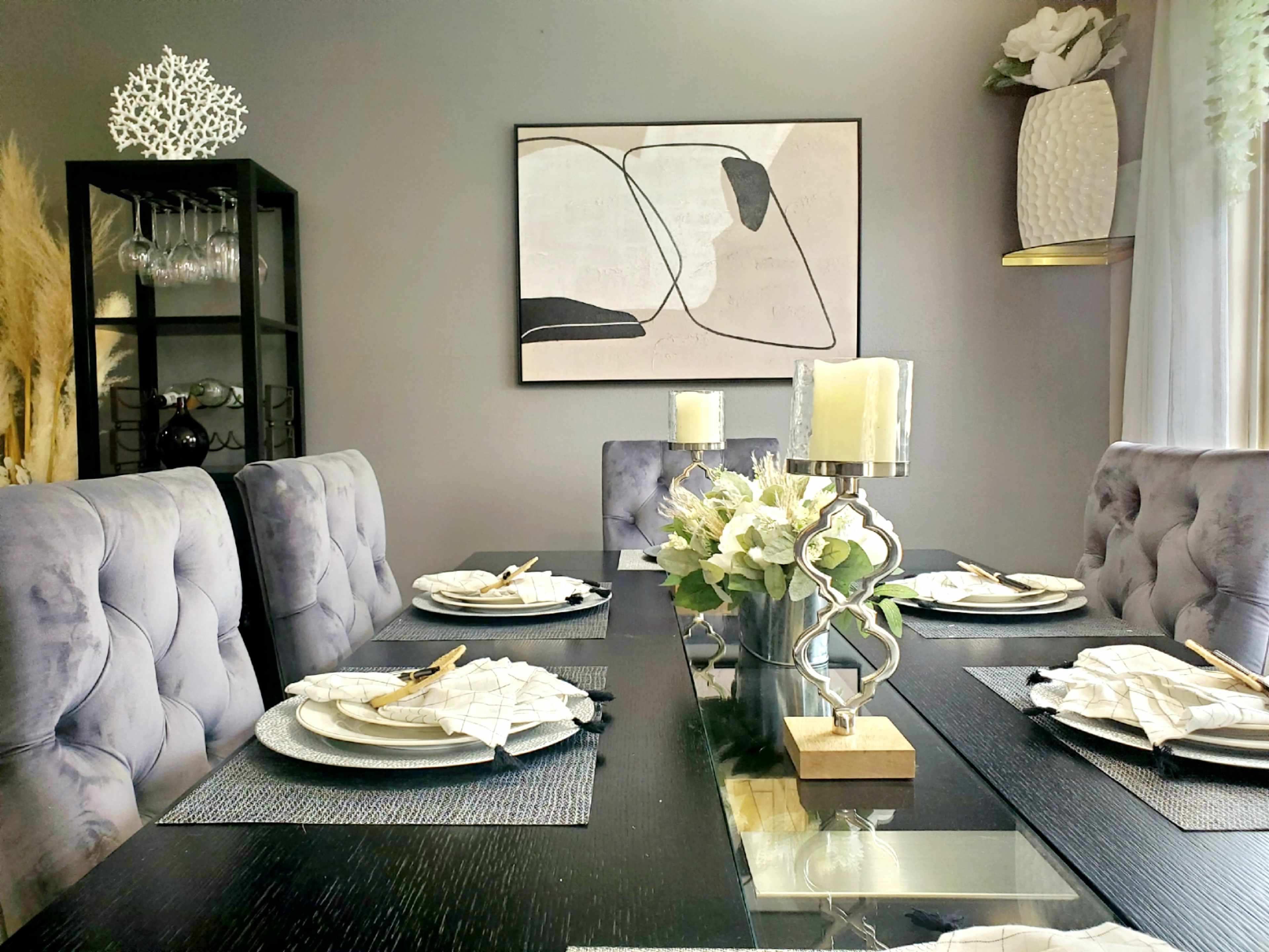 A dining room table set for a meal, featuring elegant dishes, napkins, and floral arrangements, with a modern artwork displayed on the wall above.