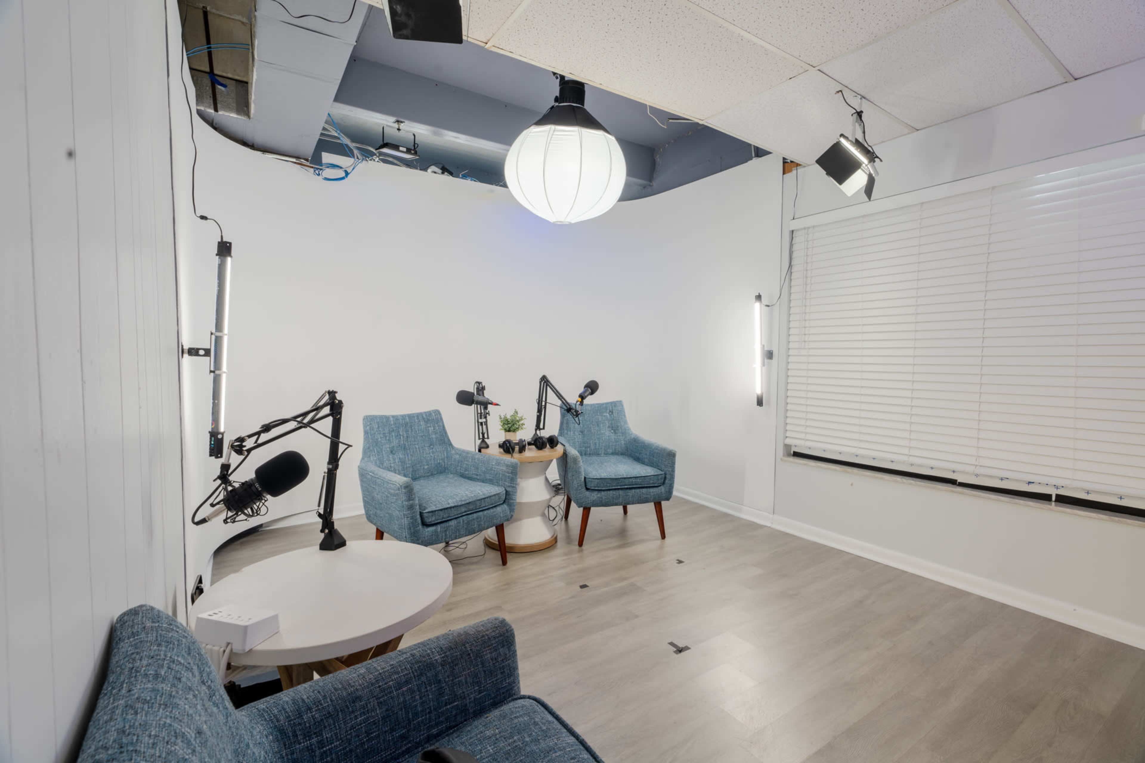 A minimalistic room with two blue chairs, a small table, and studio lighting, ready for a recording session.