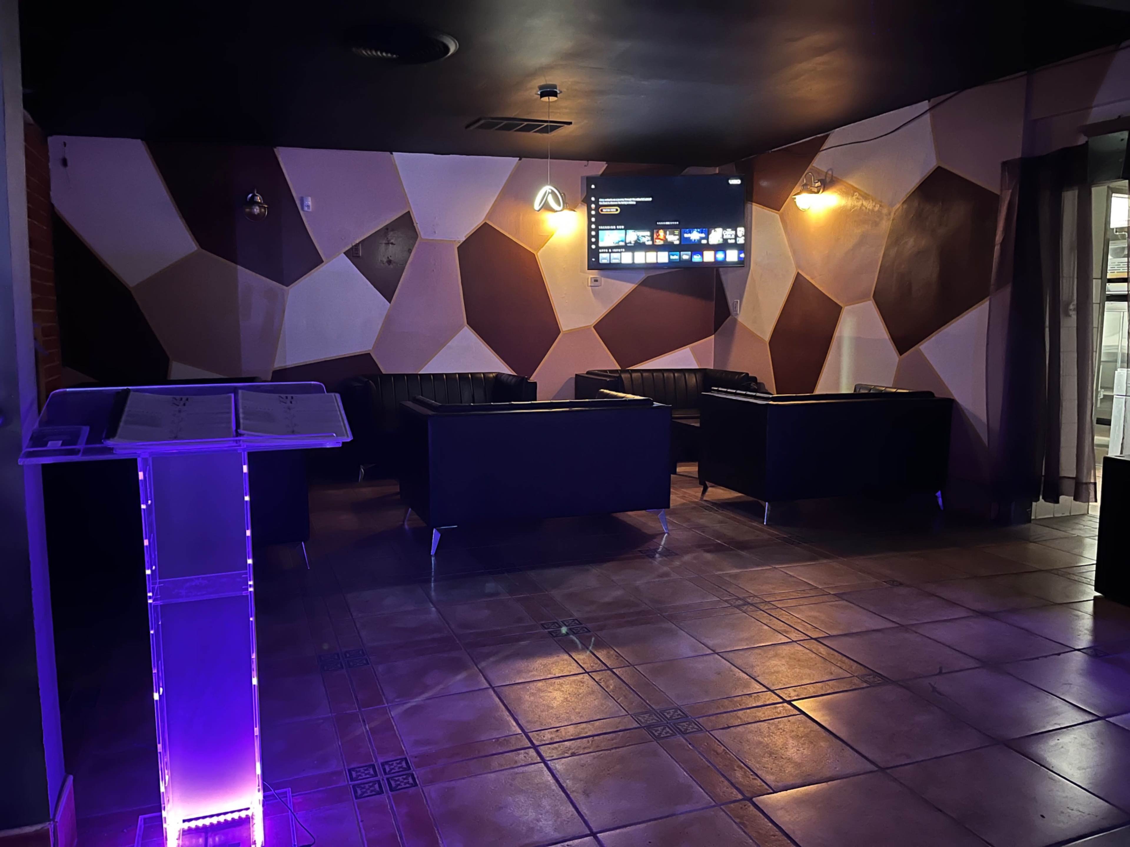 A modern lounge area with black sofas arranged around a flat-screen TV on a textured wall.