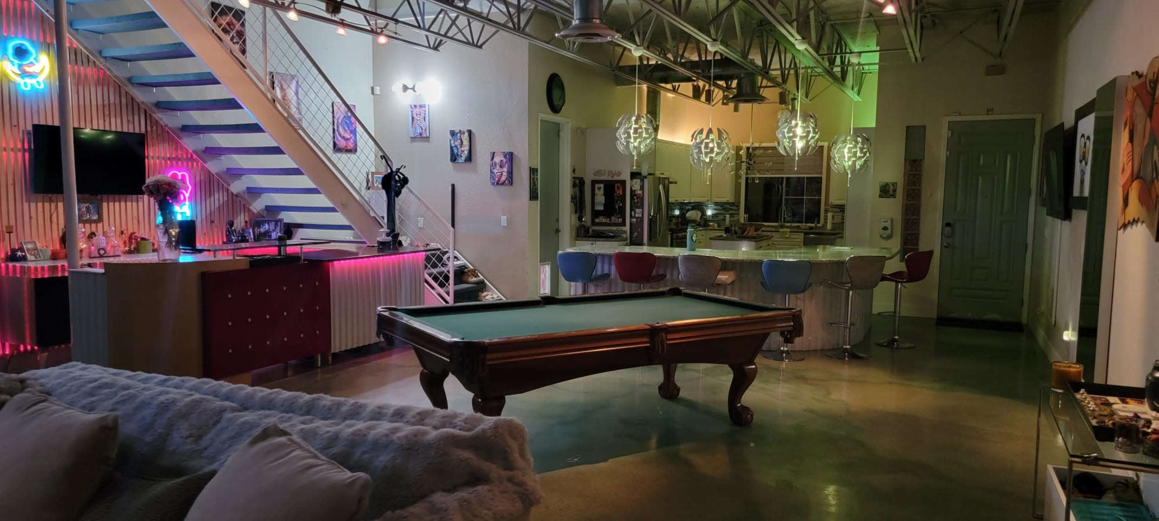 A modern, open-concept lounge area featuring a pool table, a kitchen with bar seating, and decorative lighting.