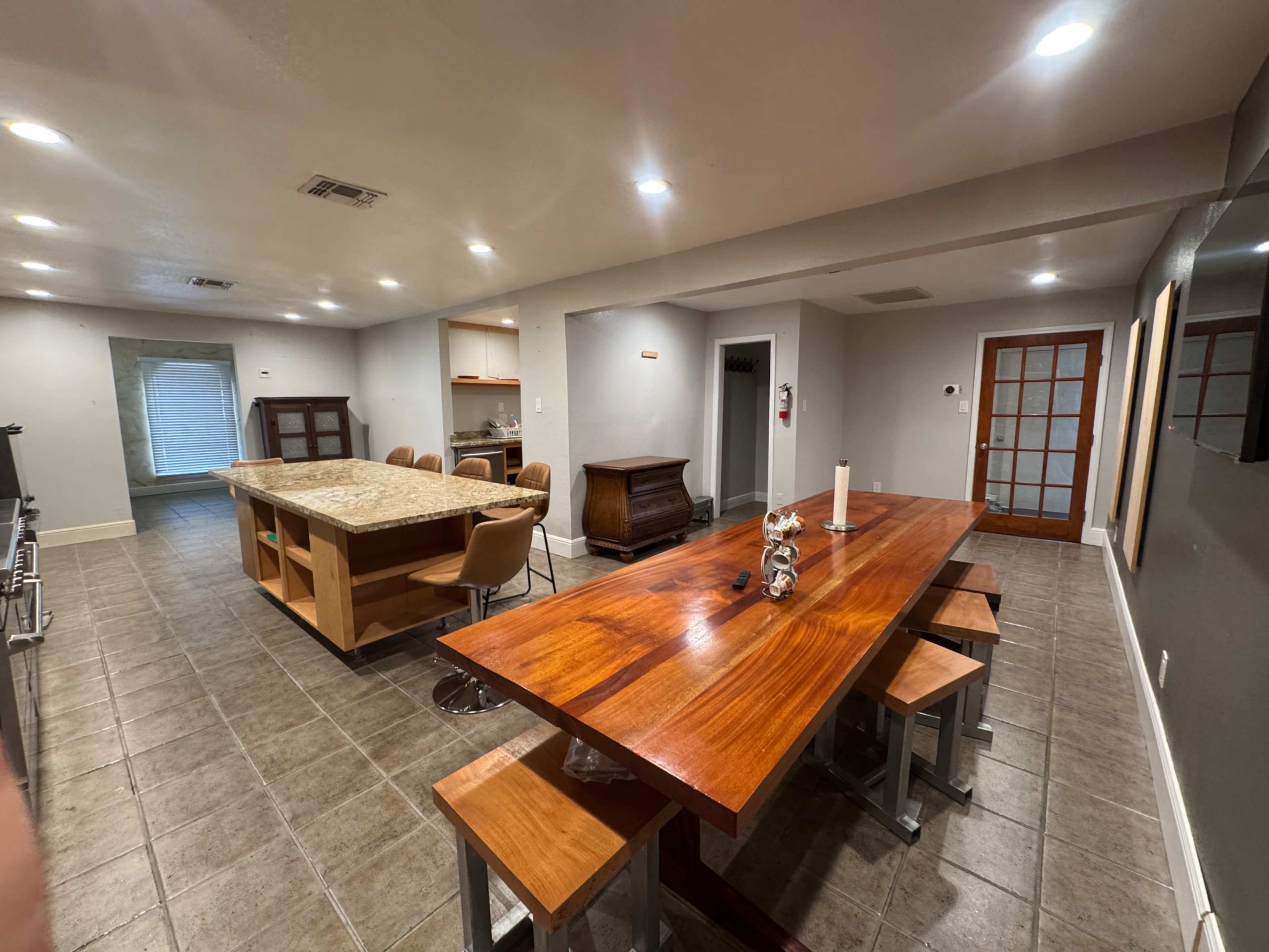 The image shows a spacious kitchen and dining area with modern furnishings, including a large wooden dining table and a kitchen island with bar seating.
