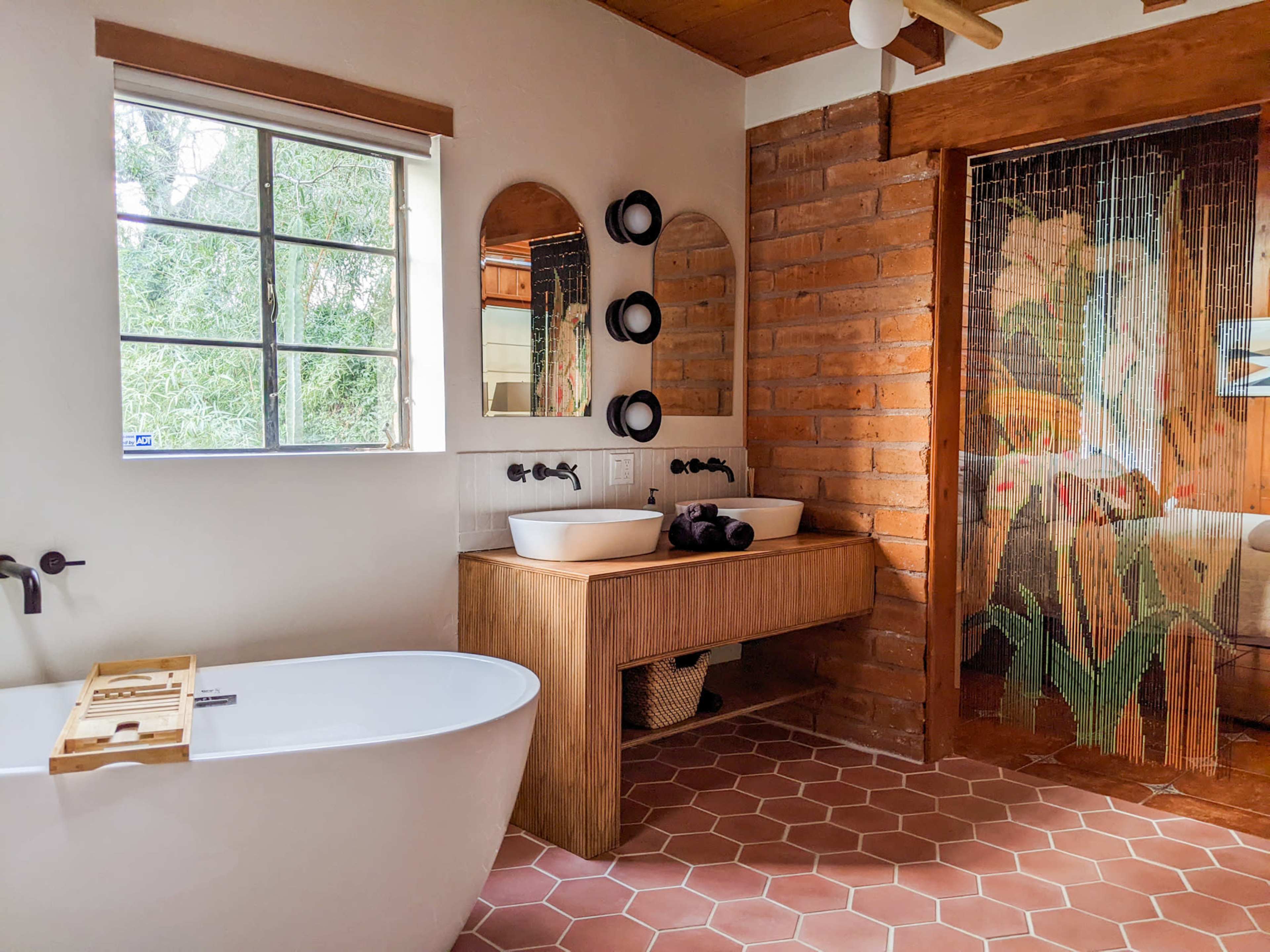 The scene features a modern bathroom with a freestanding bathtub, dual sinks on a wooden vanity, and a glass door adorned with a floral design.