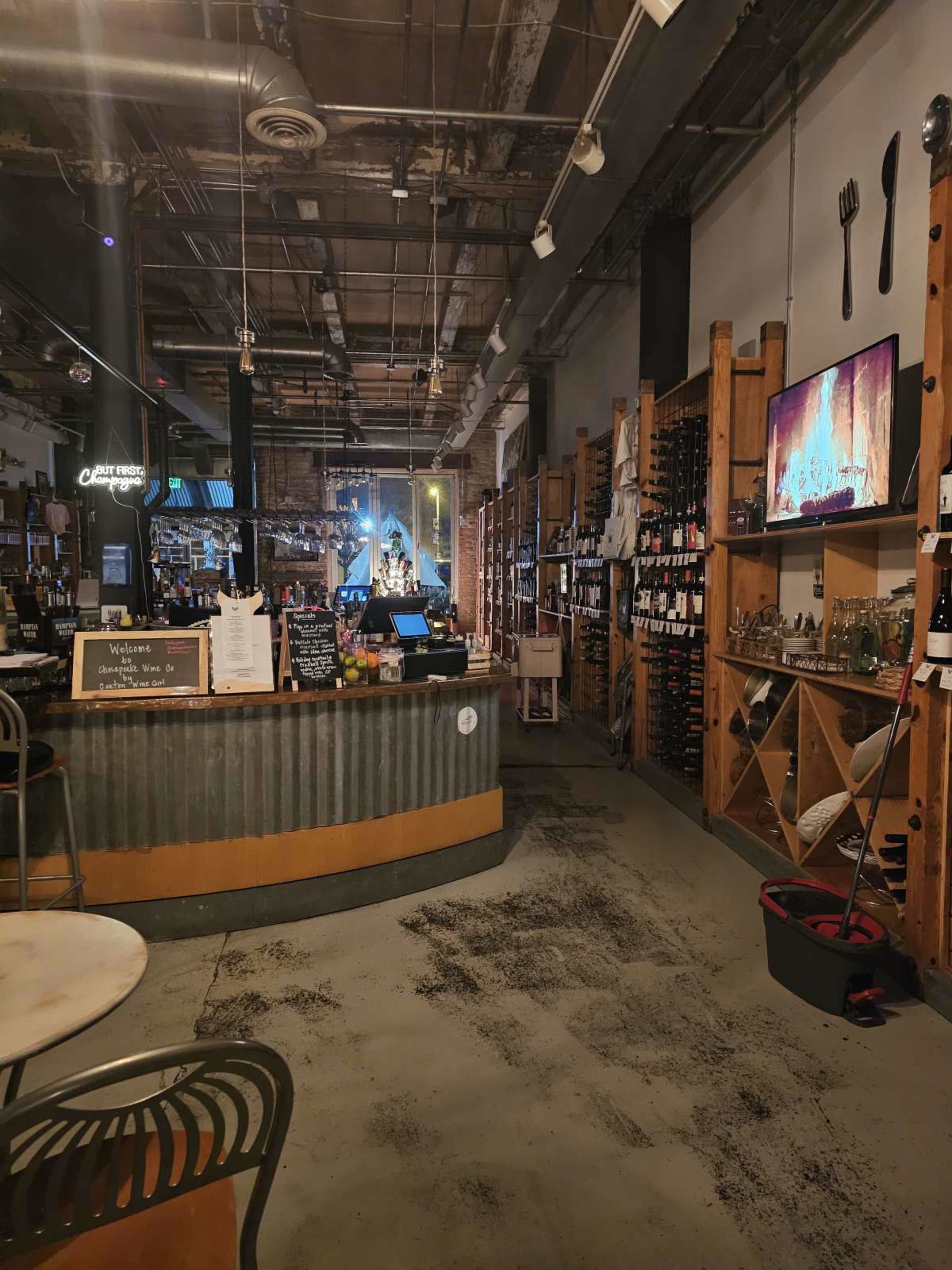 The image shows the interior of a wine shop with wooden shelving filled with wine bottles and a circular bar area at the front.